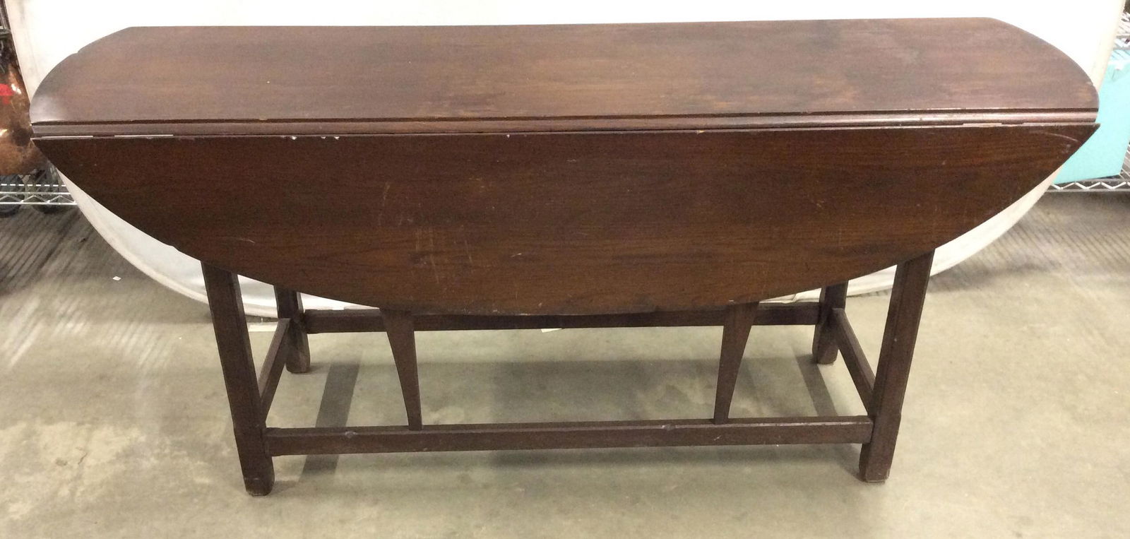 Antique Drop Leaf Sofa Table: This is an antique drop leaf table, the table is wooden and is cherry toned in color. The legs of the table are joined by stretchers, and the sections supporting the leaves sport an almost Cabriole-li