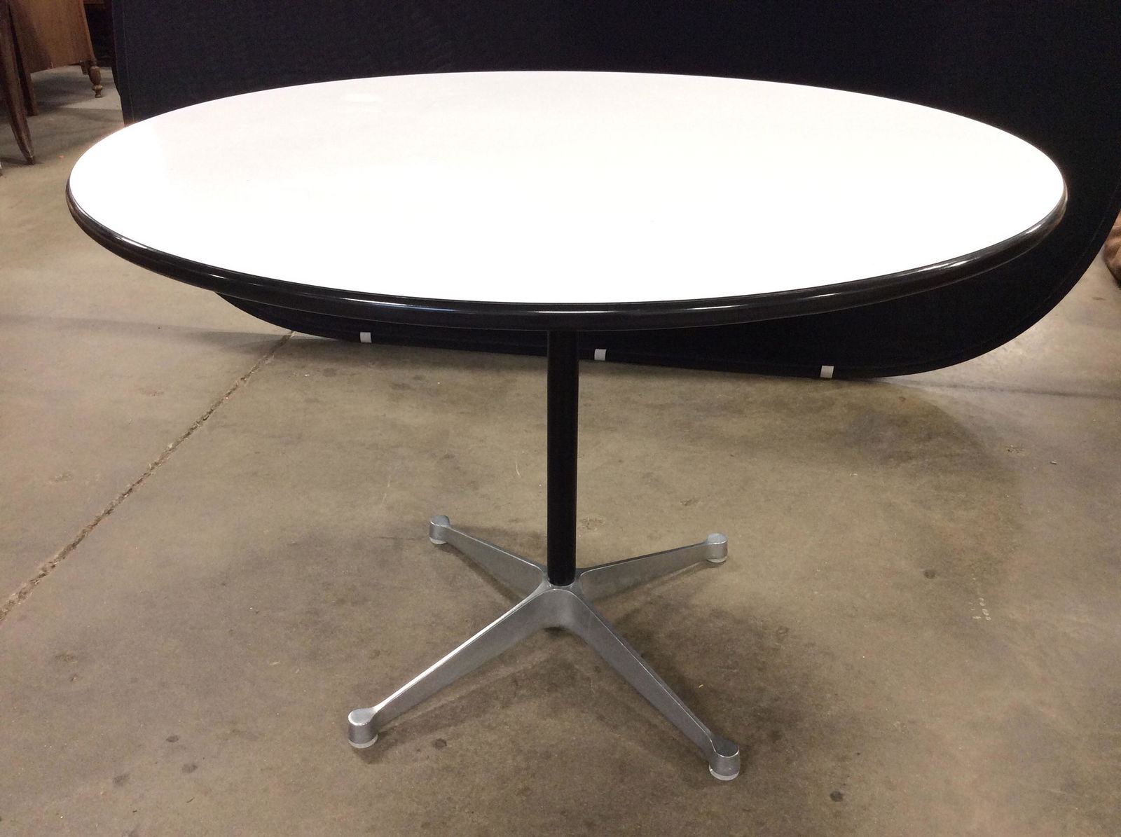 Mid Century Modern Herman Miller Charles Eames Table: A mid century Eames Aluminum group dining table by Herman Miller. The table features a round, white laminate top above a cylindrical, steel support ending in a four-point, aluminum base. Marked on und