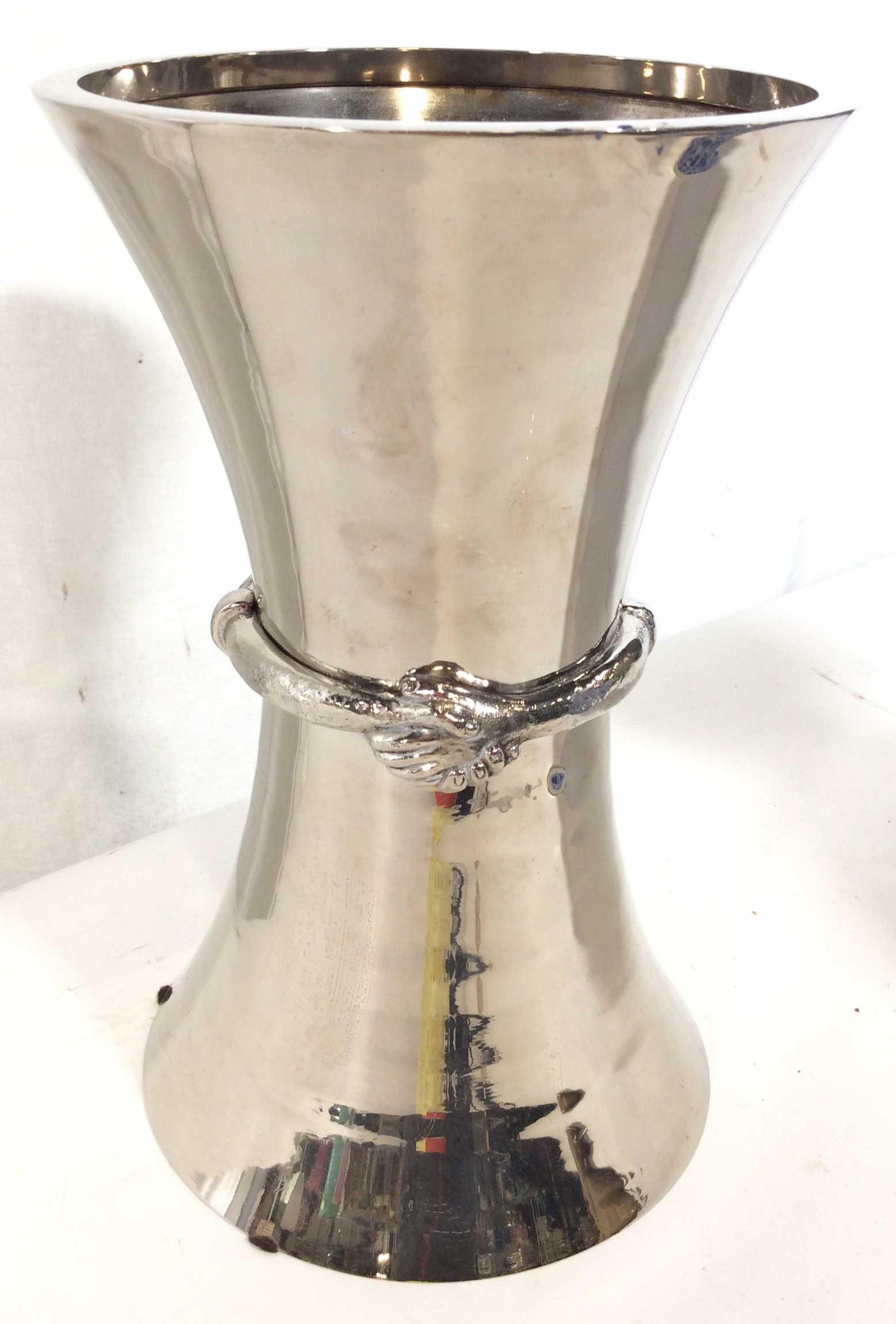 Michael Aram Clasped Hands Tall Vase: Silver-tone metal Michael Aram tall vase with clasped hands motif at center and brand stamp at underside. Measures approx 13 in tall by 8 in in diameter. Some discoloration and wear. tableware tableto
