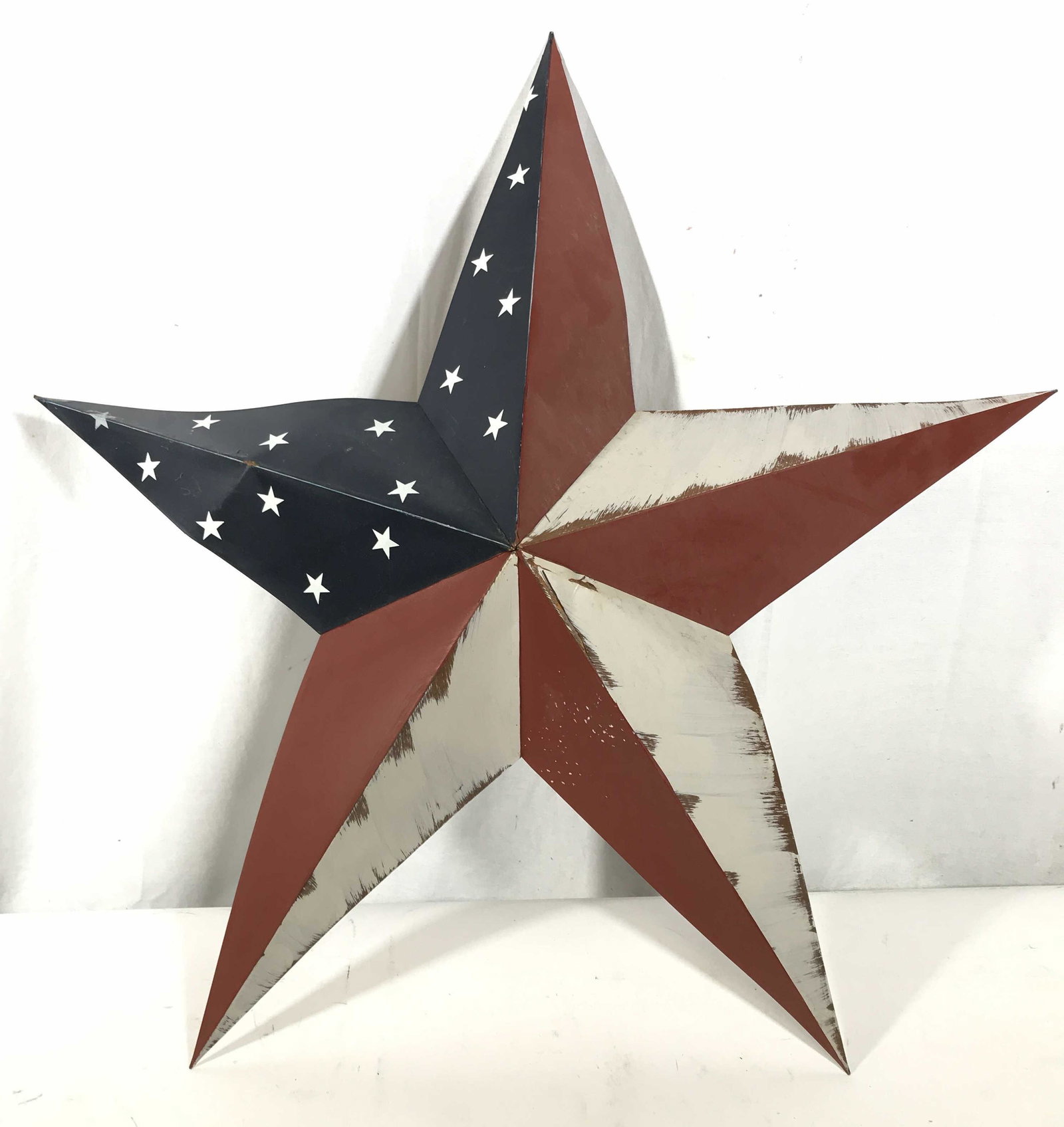 Americana Metal Star Wall Hanging: metal dimensional star, wall hanging, red white and Blue American Flag design, evident wear discoloration and cracking of finish, warping to metal, measures approximately 29 1/2 in by 29 in, Beach Wal