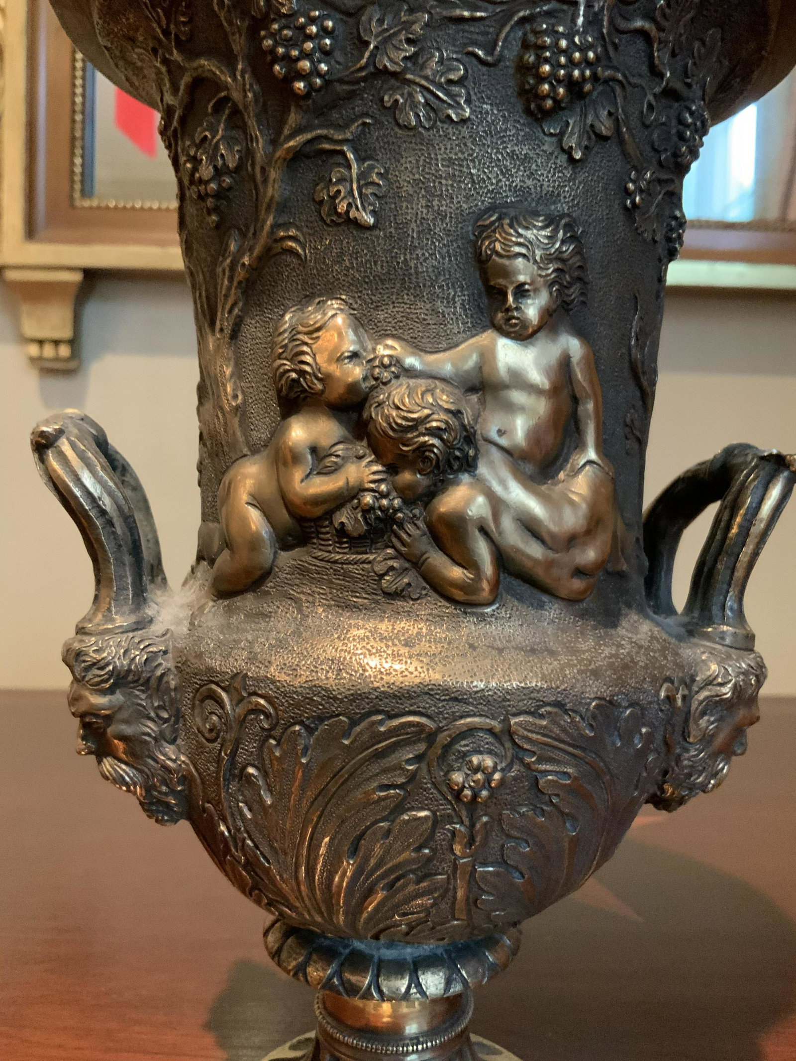 Antique Bronze Toned Heavy Relief Urn: Antique heavy Metal urn possibly bronze, bronze tone, possibly brass, heavy weight, small chip, heavy relief of cherubs,puttis, angels, feeding grapes, gargoyle heads at base of jug handles, double ha