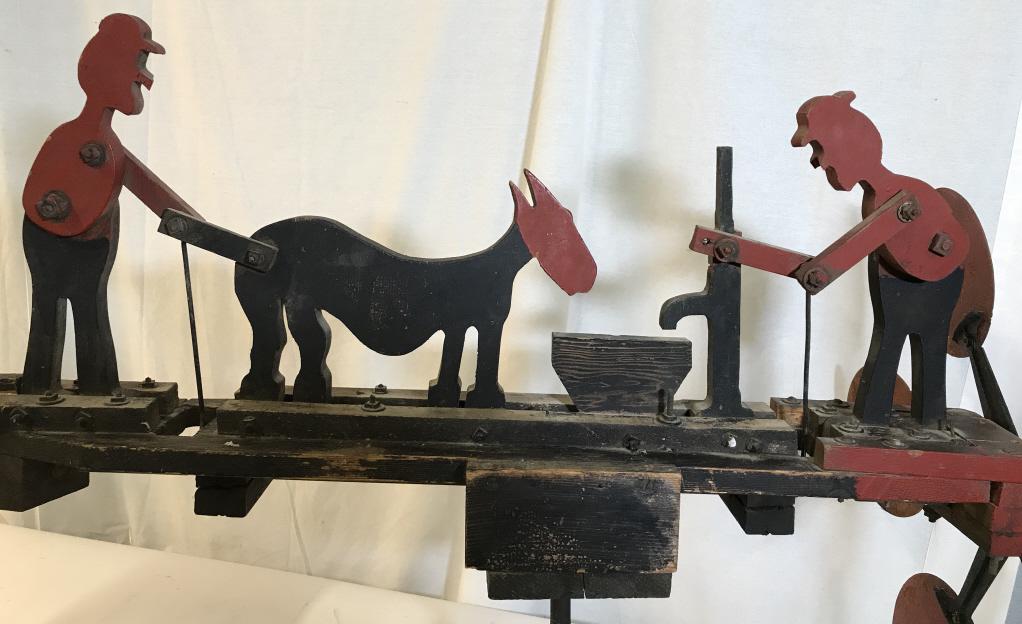Antique Folk Art Farming Figural Whirligig: Whimsical Figural whirligig with two men and a donkey. One man filling a trough with water pump for a mule, the other man pumping the mules tail. Comes in 2 pieces, art rests on wooden base with 2 iro