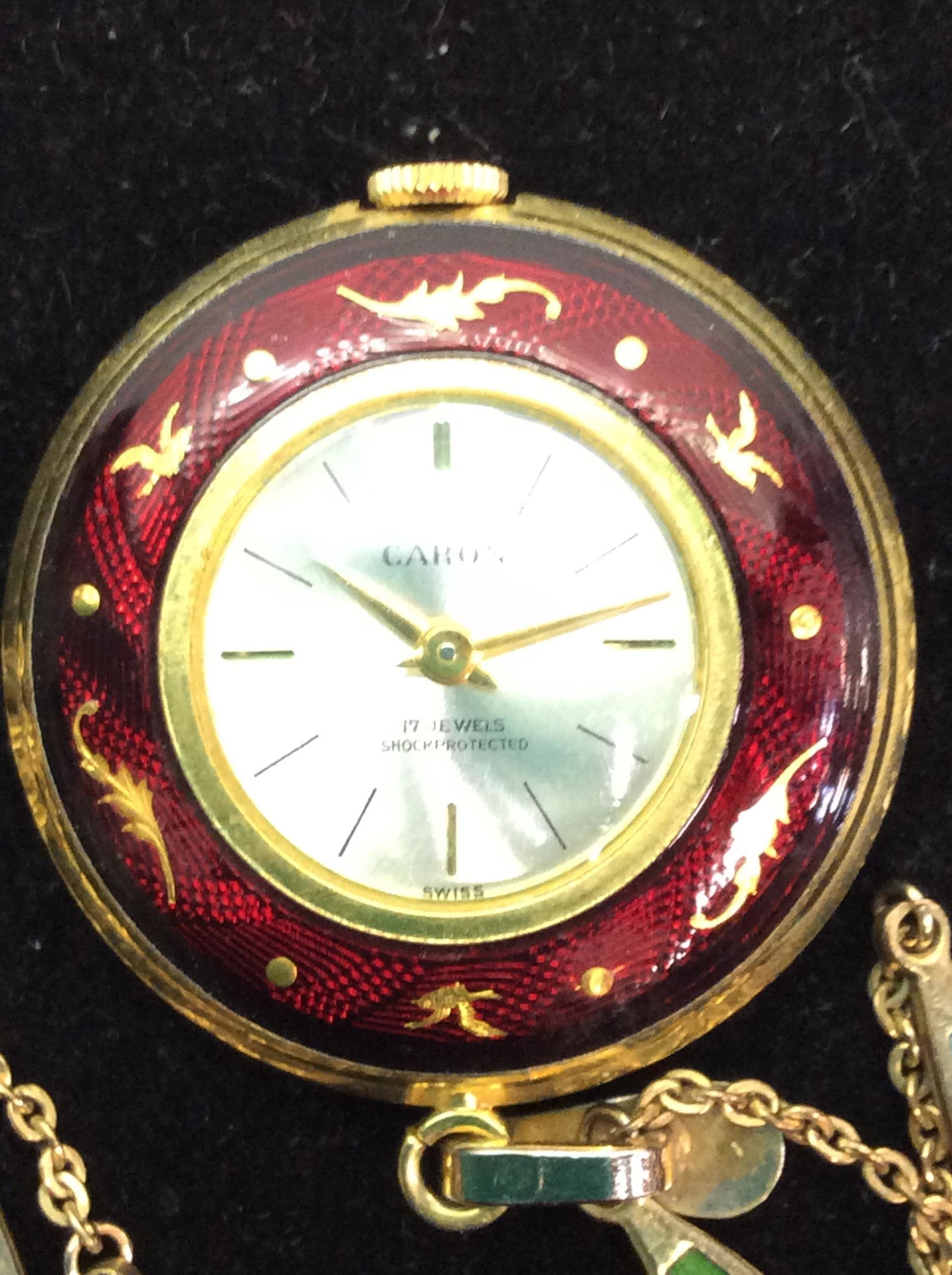 CARON enameled Watch Pendant Aurea Necklace: Vintage piece. Gold Tn Chain with enameled links, link near clasp reads ‘Aurea’ with an impressed ‘AR’ symbol. C spring clasp. Caron watch pendant, 1 in. Reads 17 Jewels Shockprotected, Swiss.