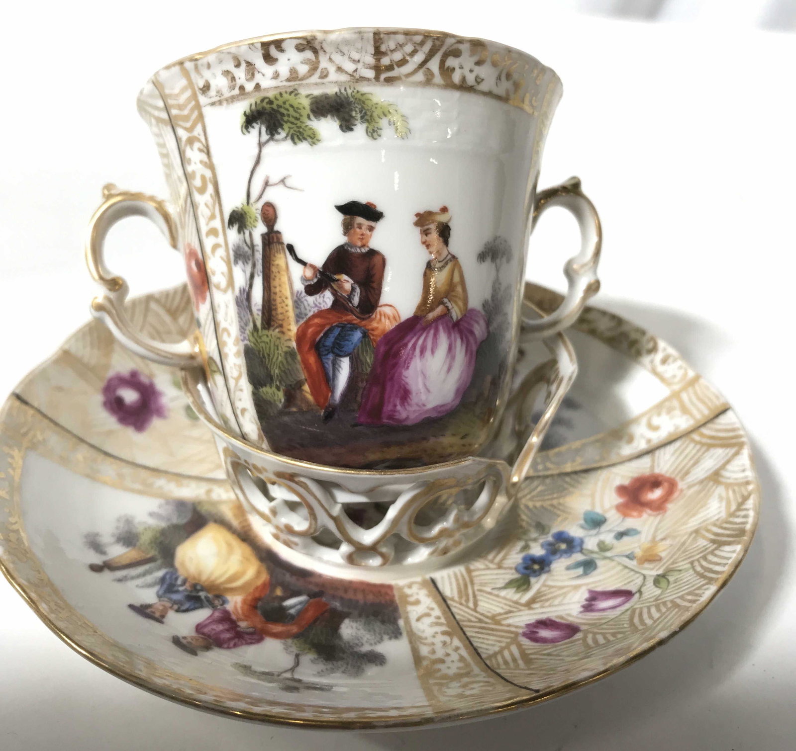 Antique Hand Painted Cup and Saucer Set: Antique possibly vintage painted porcelain with gold detailing, Victorian scenes and trademarked underside, saucer diameter app 5.5 inches, height double handled cup app 3 inches tableware, tabletop a