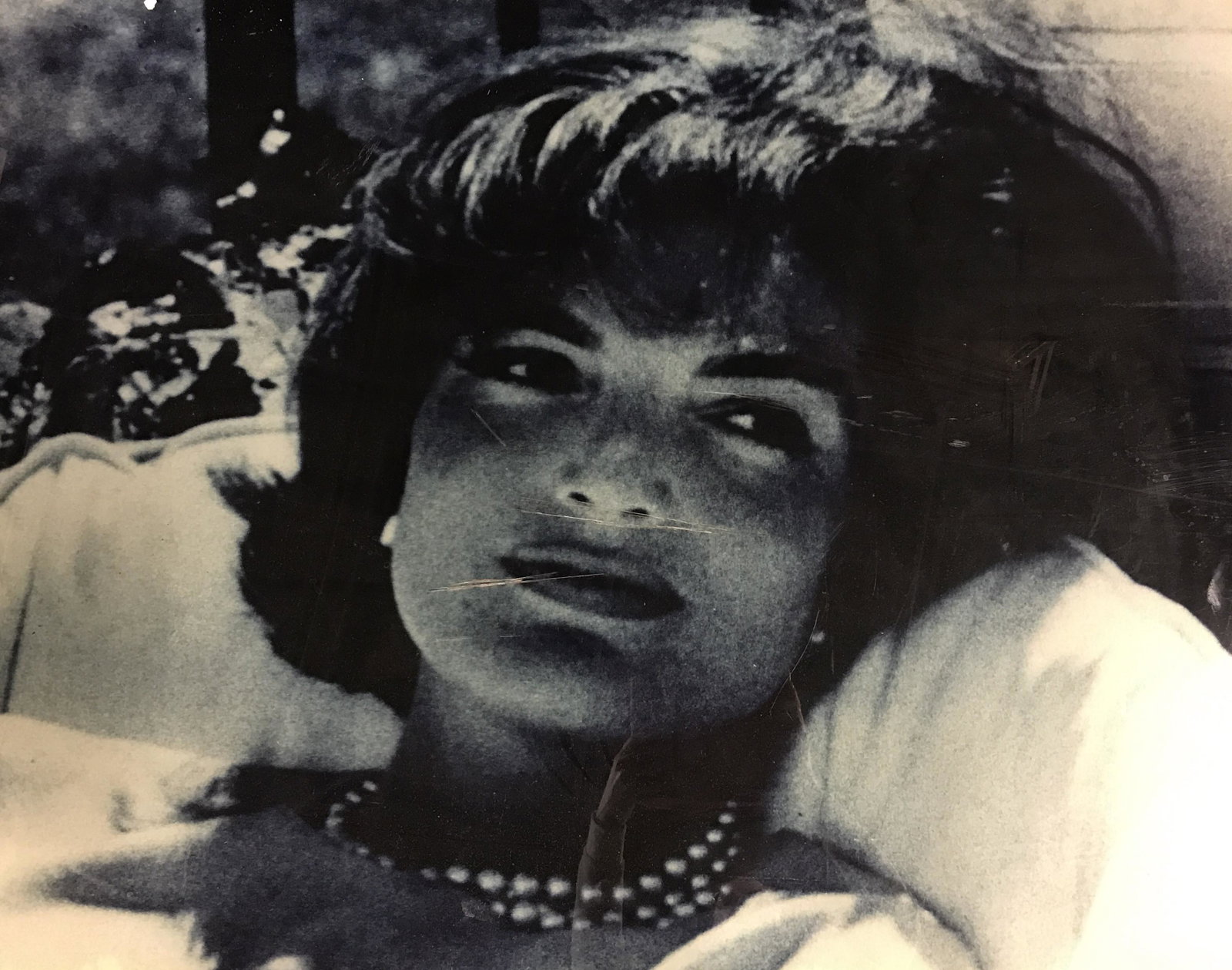 Oversized Photo Print of Jackie Kennedy: This is a print adhered to thick plexi glass of Jaqueline Kennedy lounging on a chair wearing her famous pearls. Size is 44 in. by 34 1/4 in. Scratches to back show through front of plexiglass. Black