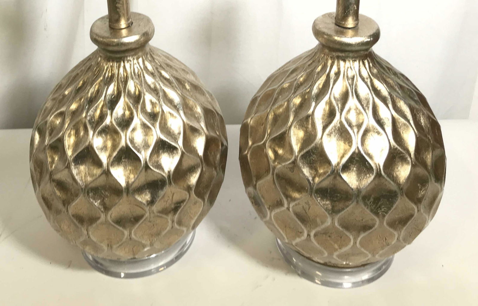 Pair Gold Toned Tabletop Lamps: This is a pair of gold toned table top lamps. The pieces are oblong in shape, with a cratered texture. There is wear present on the piece consistent with age and use. The largest piece measures approx
