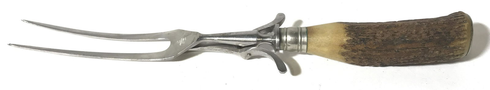 Vintage Antler Style Serving Fork, Germany: This lot includes a vintage serving fork, the handle is crafted to resemble an antler, A clamp is on the fork, allowing the fork to grip whatever is being skewered. The piece measures approx 11 inches