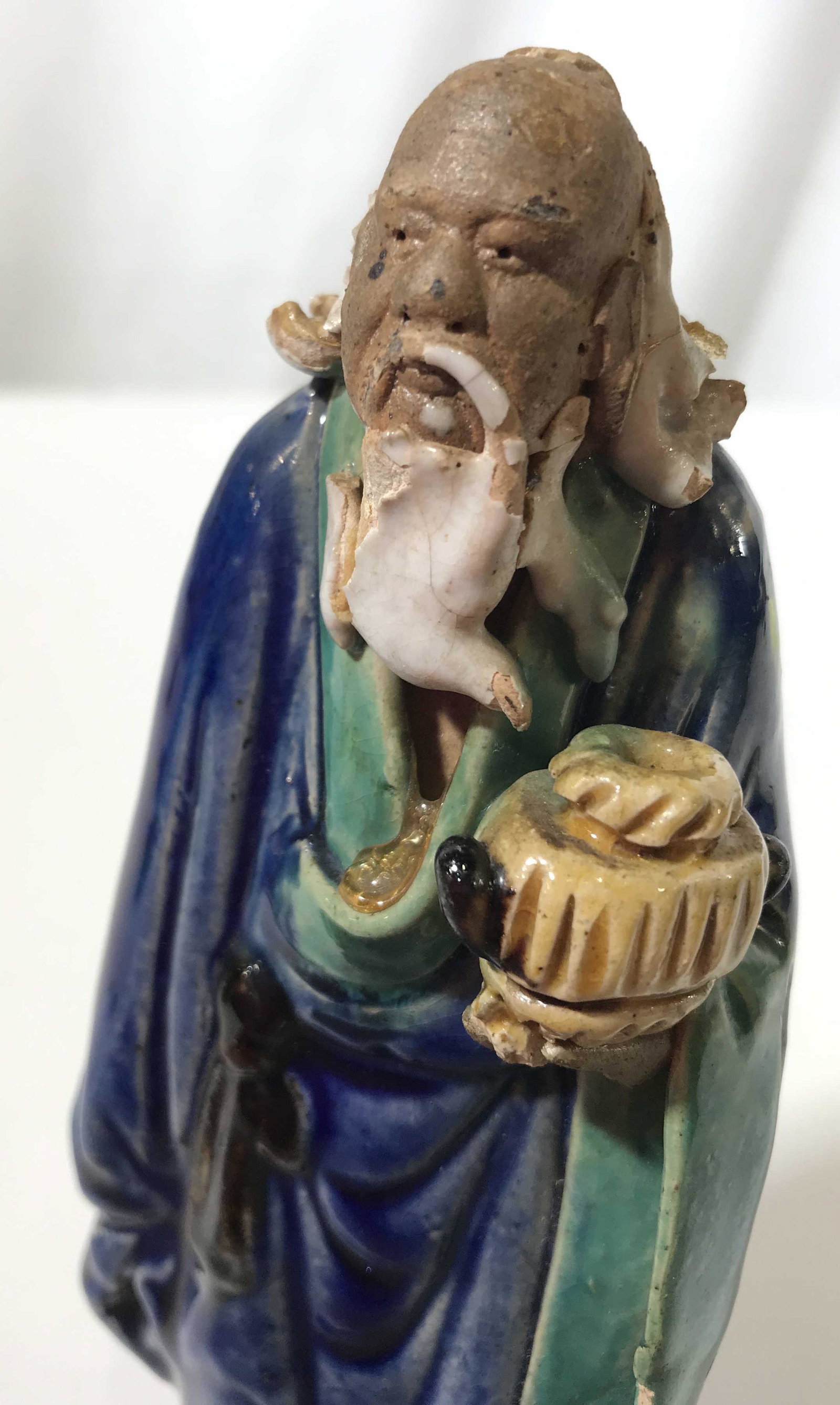 Vintage Handmade Earthenware Asian Male Figure: This piece is a handmade earthen ware figure. The piece resembles an asian male holding an urn, the piece is hand painted and is colored in orange, cobalt, and teal tones. The figure measures approx 5