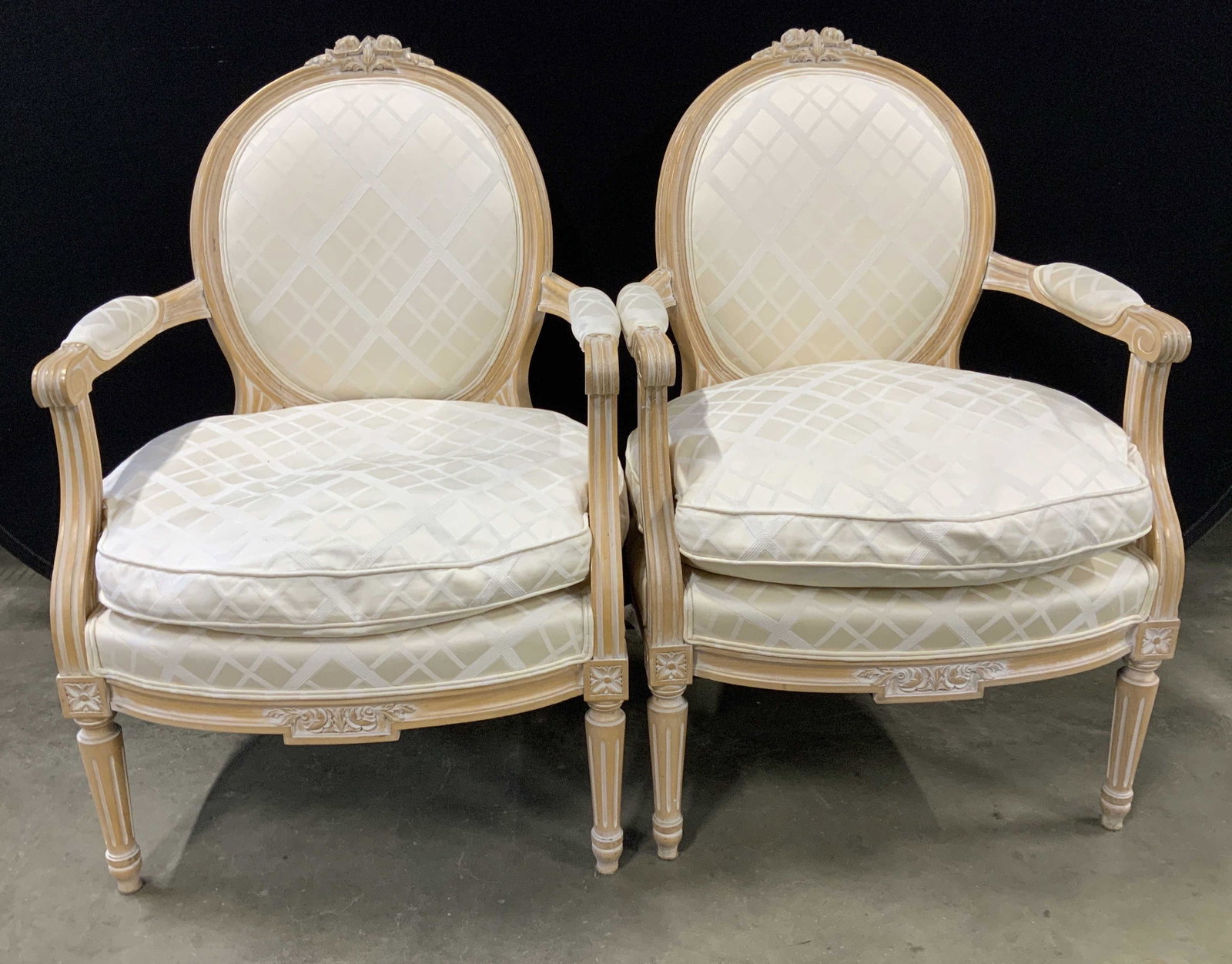 Pair Country French Style Bergere Chair: Upholstered armchairs with oval backs, partial upholstered arms and loose cushion seats, one cushion has stain, light wood frames with tapered receded legs and floral crown to backs, each measures ht 