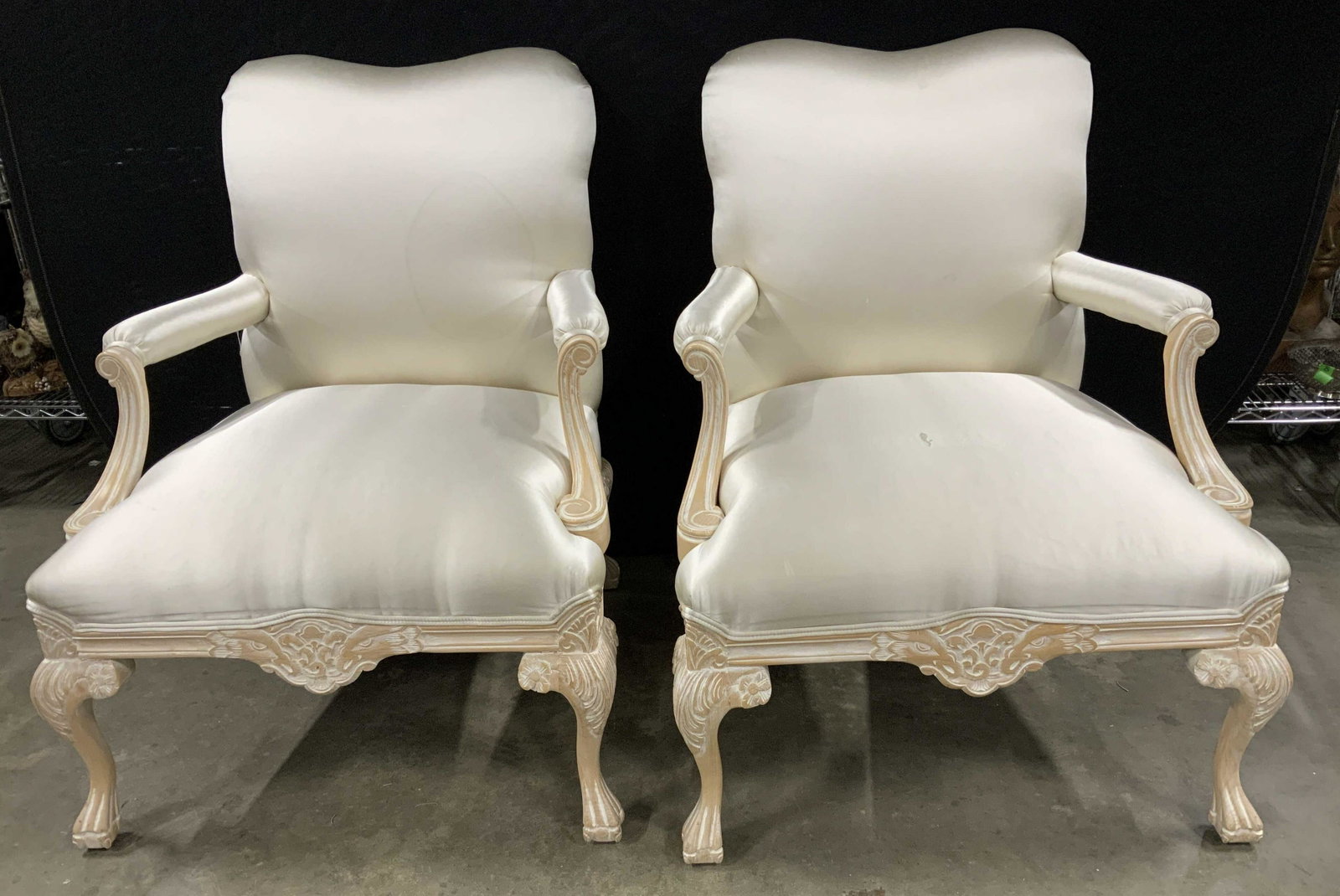 Pair Wood Framed Upholstered Bergere Chairs: Pair of Country French style white washed wood frames, floral motif at seat apron, scrolled and paw feet, extra wide arm chairs each upholstered in cream silk satin, upholstery has stains and discolor