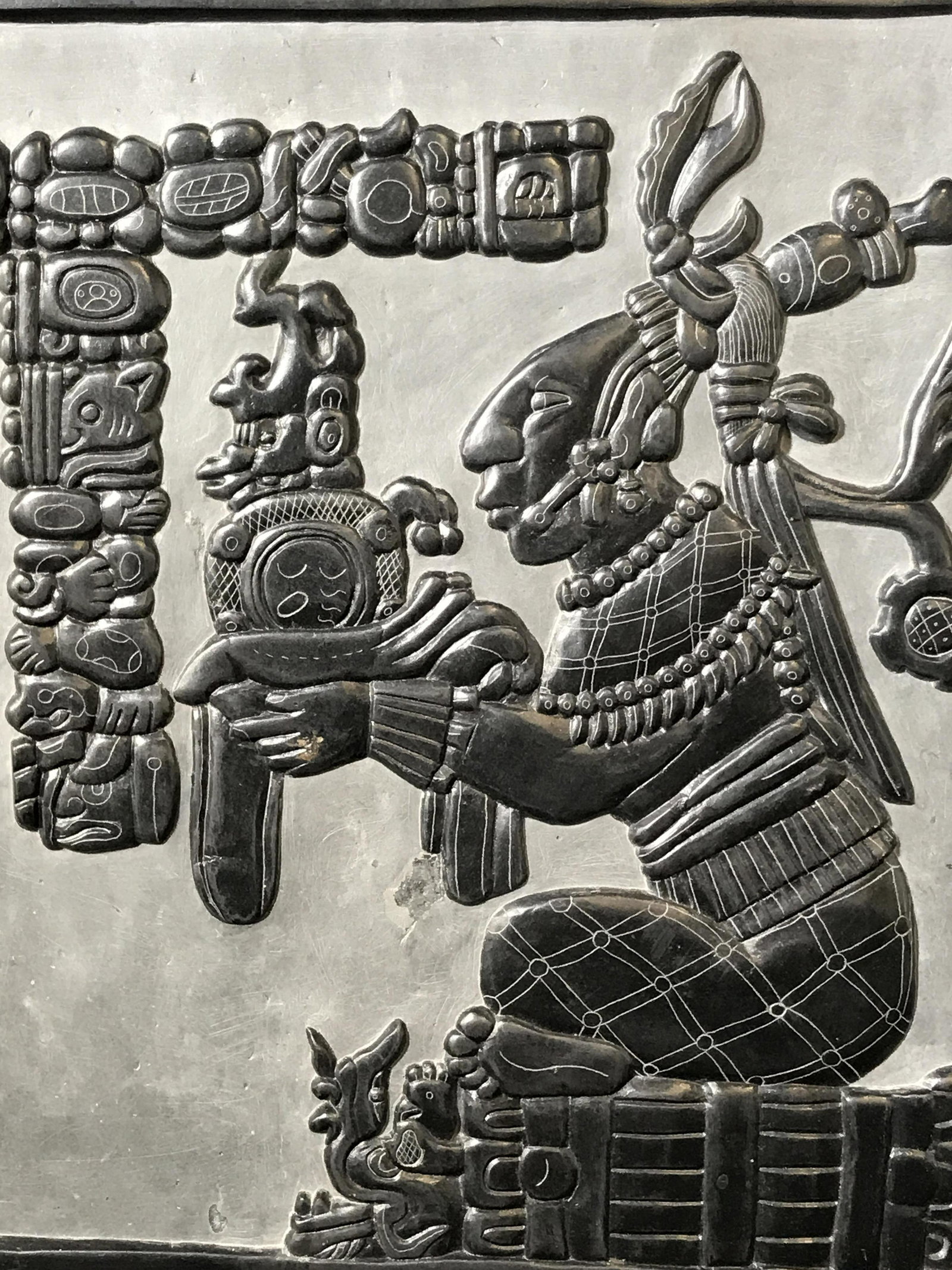 Mayan Style Carving in Black Stone: Mayan carving on black stone possibly black marble, no apparent signature, carving shows a man seated cross legged holding a large object possibly an offering, carving includes anthropomorphic designs