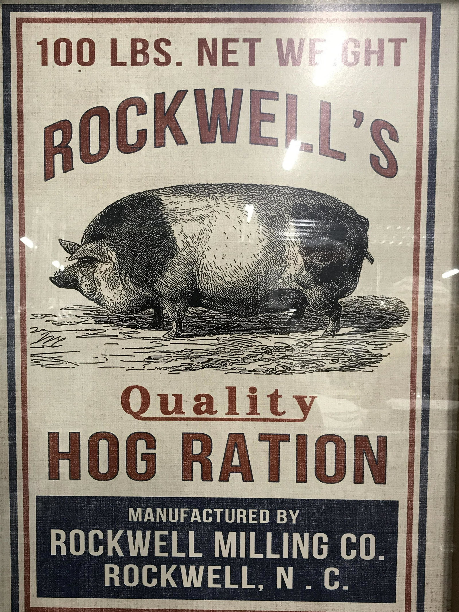 Framed Advertisement Rockwell’s Quality Hog Ration: Framed Advertisement, ad displays text and the head of a chicken on a white and blue background, text on ad from top to bottom reads ‘100 LBS., Rockwell’s Quality Hog Ration, Manufactured by Rockw