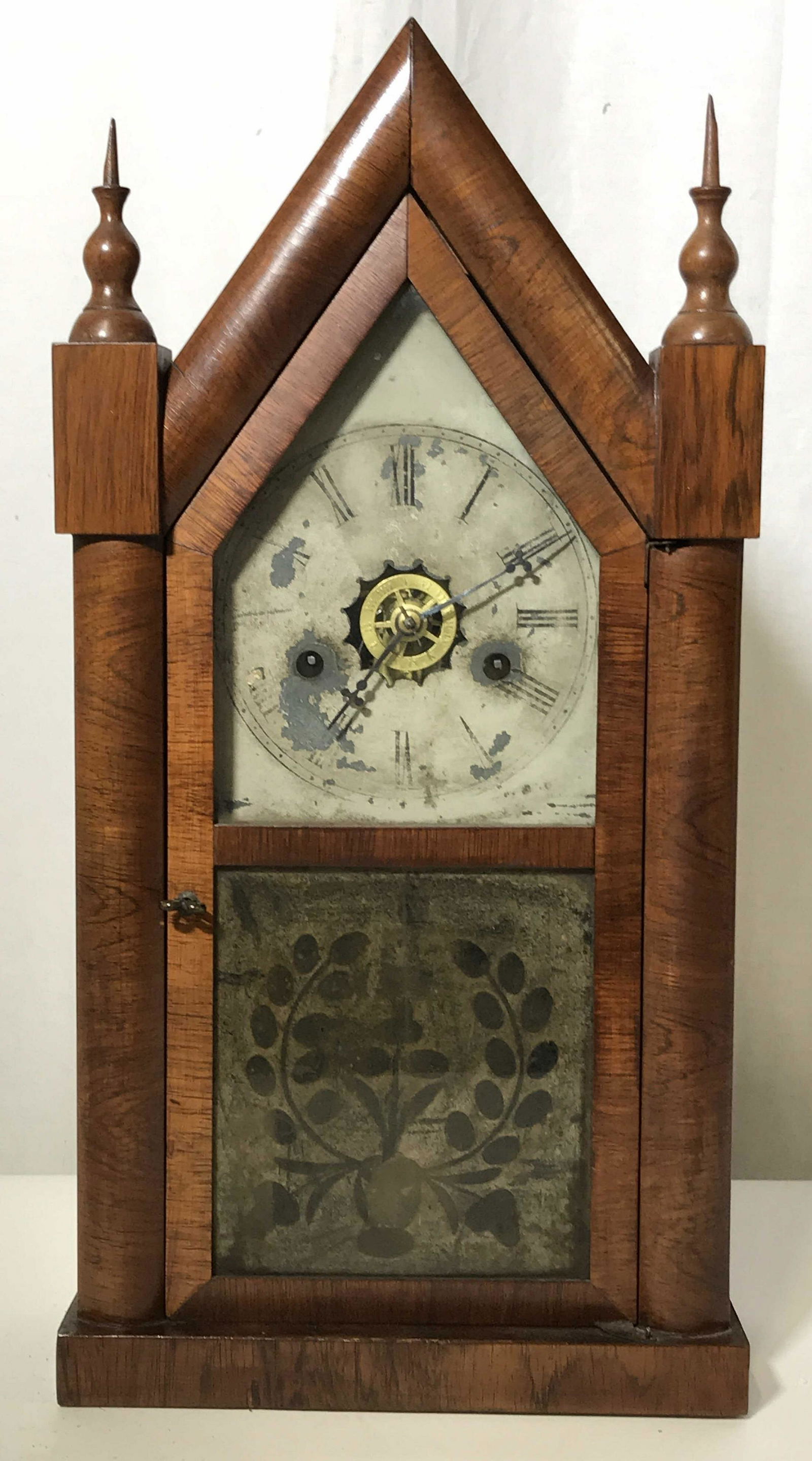 Vintage Wooden Pendulum Clock: Vintage possibly antique, wooden pendulum clock, made of a Chestnut colored wood With gothic spires on the top, glass paneled door in front with the lower panel painted with floral designs, handle doo