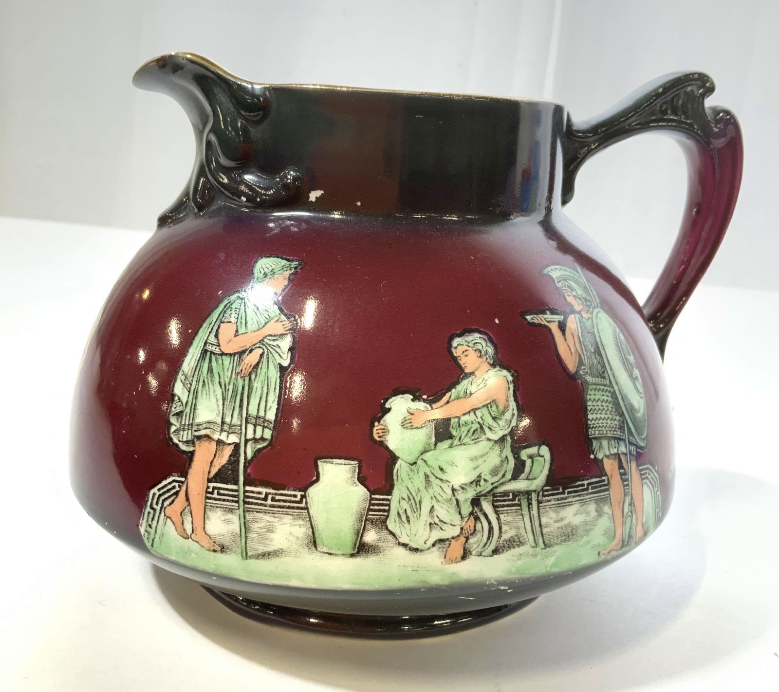 HAYNES BALT collectible Porcelain Pitcher: Porcelain ceramic pitcher, vase, vessel, table ware, violet crimson and green tones with Grecian Roman Figurals, measures ht 7 inches, handle to spout app 8 inches, has hairline crack inside