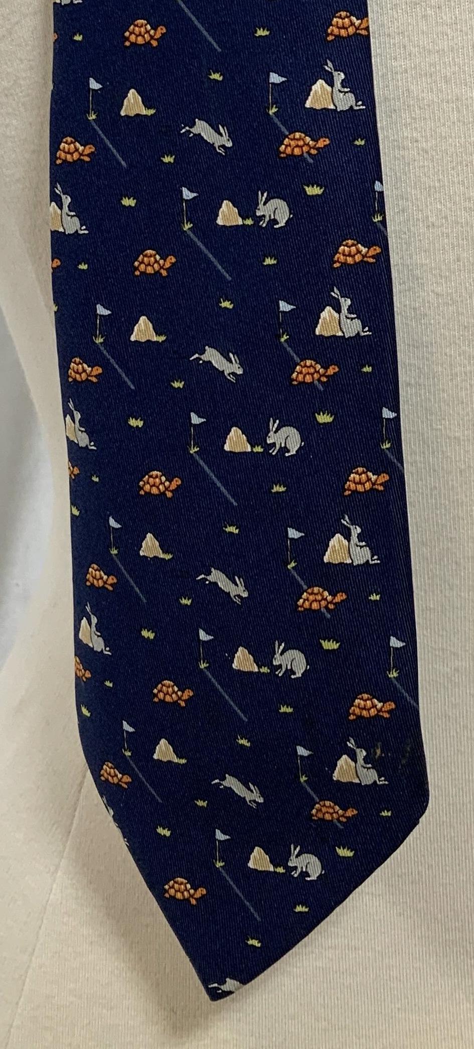 Hermès Tie, Men's Luxury Fashion accessory: Hermès tie, depicts the tortoise and the hare on a dark blue background, keeper loop reads ‘Dry Clean Only 100% Silk’, label on front of tail reads Hermès PARIS, label on reverse of tail reads �