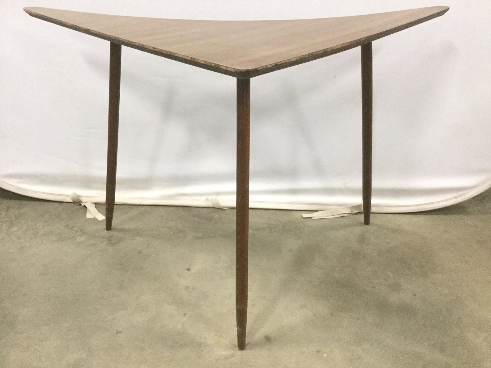 Carved Wooden Mid Century Modern Table: Table is mid century modern. Piece has 3 wooden legs. Table top has arrow shape with 1 curve side. Table is light brown toned. Table measures approximately 28 inches tall 47 inches long 26 inches deep