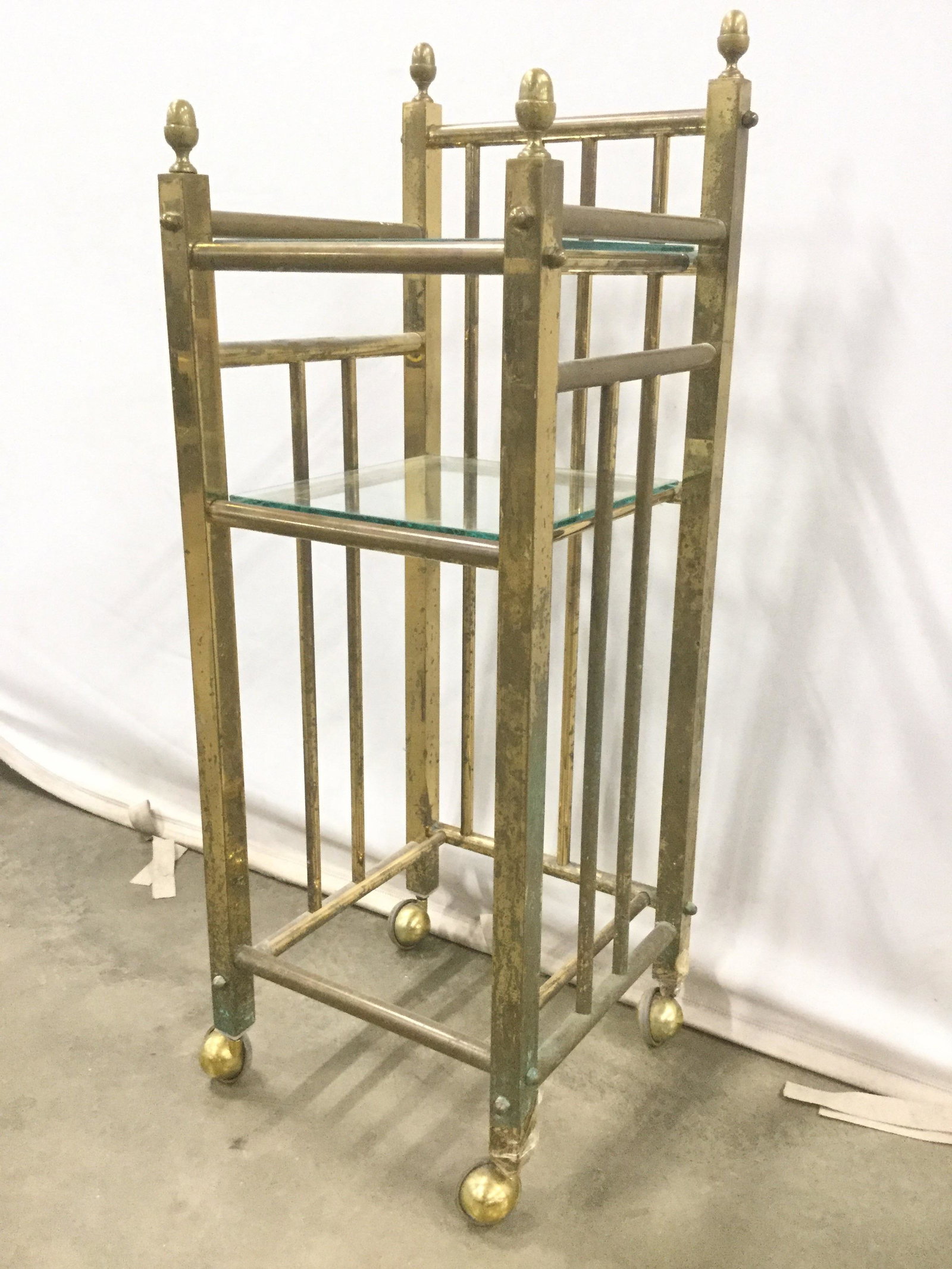 Antique Gold Toned Brass Side Table On Casters: Side table is gold toned and brass. Piece has 4 casters and 4 finial structures. Piece includes 2 glass surfaces. Measures approx 13 inches square 35 inches tall. Antique table, antique brass table, t