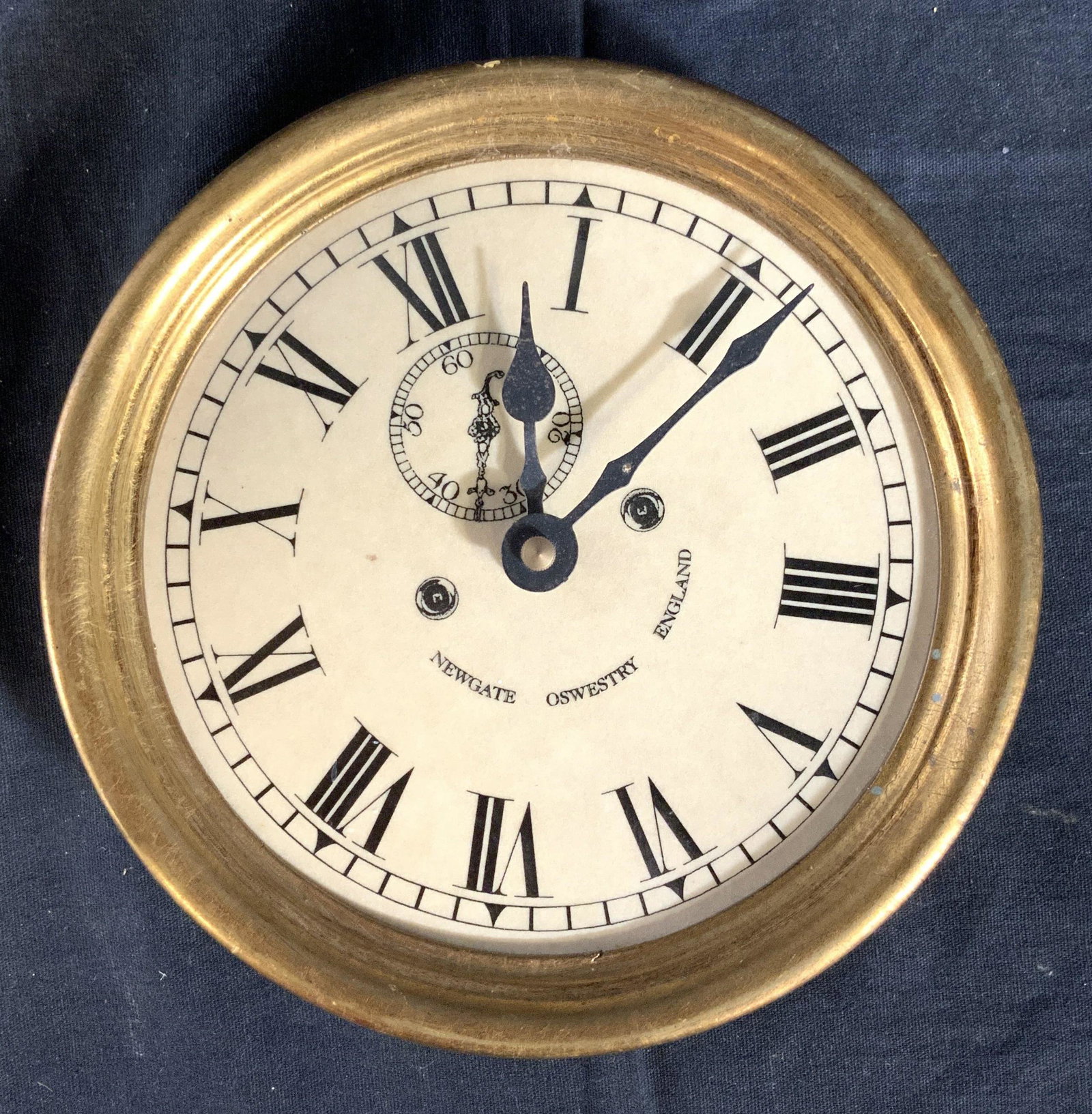 Vintage Gold Leafed Wood Wall Clock England: Vintage Circular clock, ships clock style, gold leafed framing, face reads Newgate, Oswestry England, Roman numerals on face, decorative accessory, measures diameter 7 inches depth app 2 inches, label