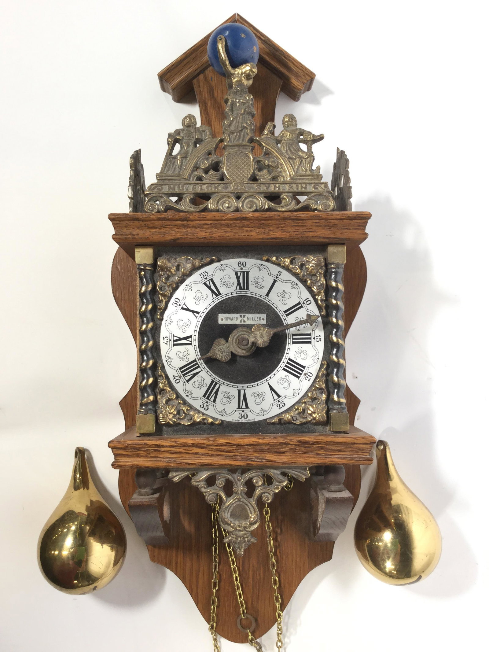 Vintage Wood & Brass HOWARD MILLER Wall Clock: Clock face is marked HOWARD MILLER, Backside is Marked MADE IN HOLLAND. Clock is wooden and brass. Piece includes 2 clock weights. Top of clock has male Atlas figure holding globe. Piece has gold tone