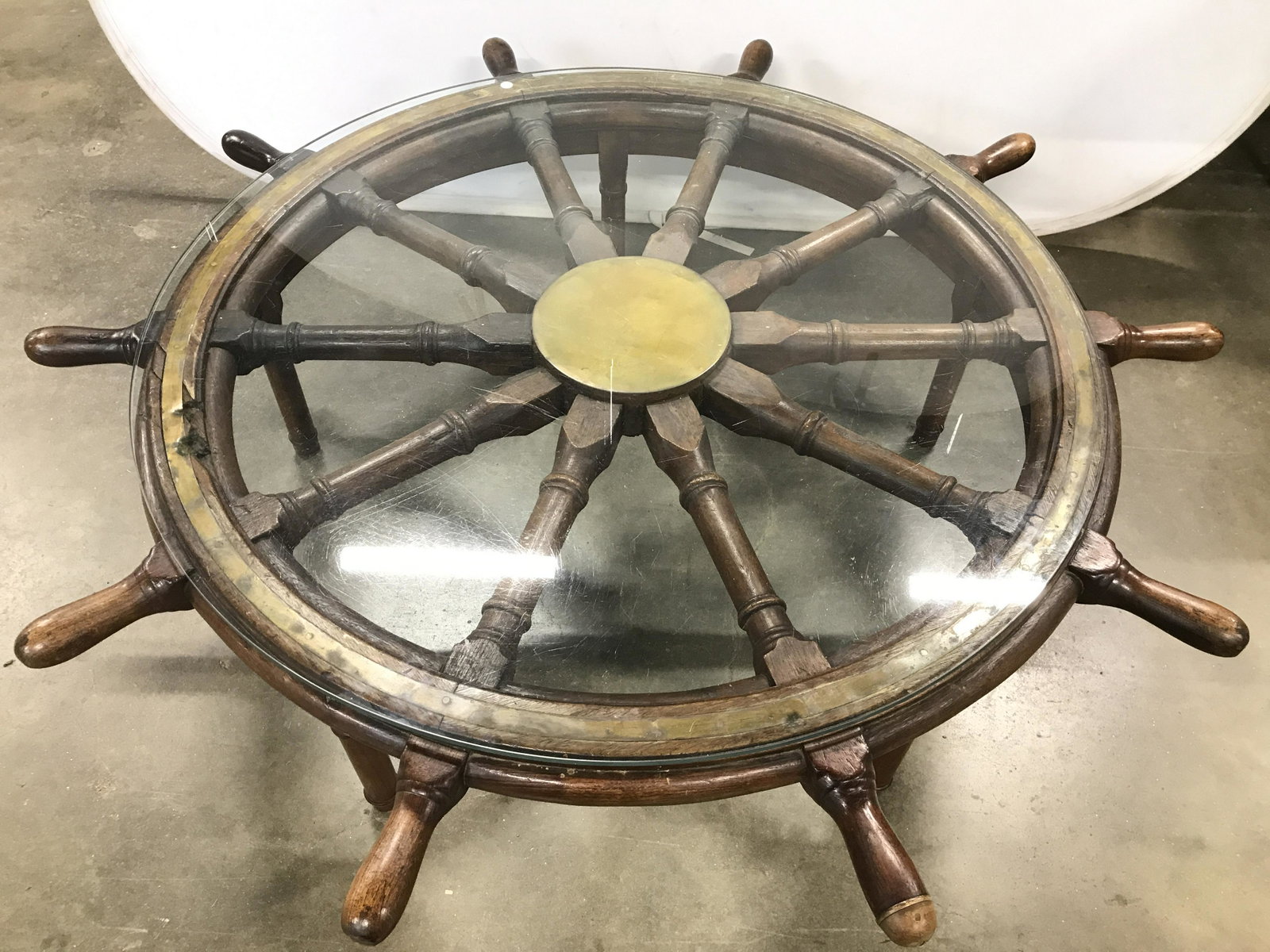 Antique Ship Wheel Glass Top Coffee Table: Coffee table is antique. Manufactured from a genuine ships wheel. Piece has carved detail. Table has 5 legs. Coffee table has glass top. Piece measures approximately 61 inches wide 19 inches tall. Cof