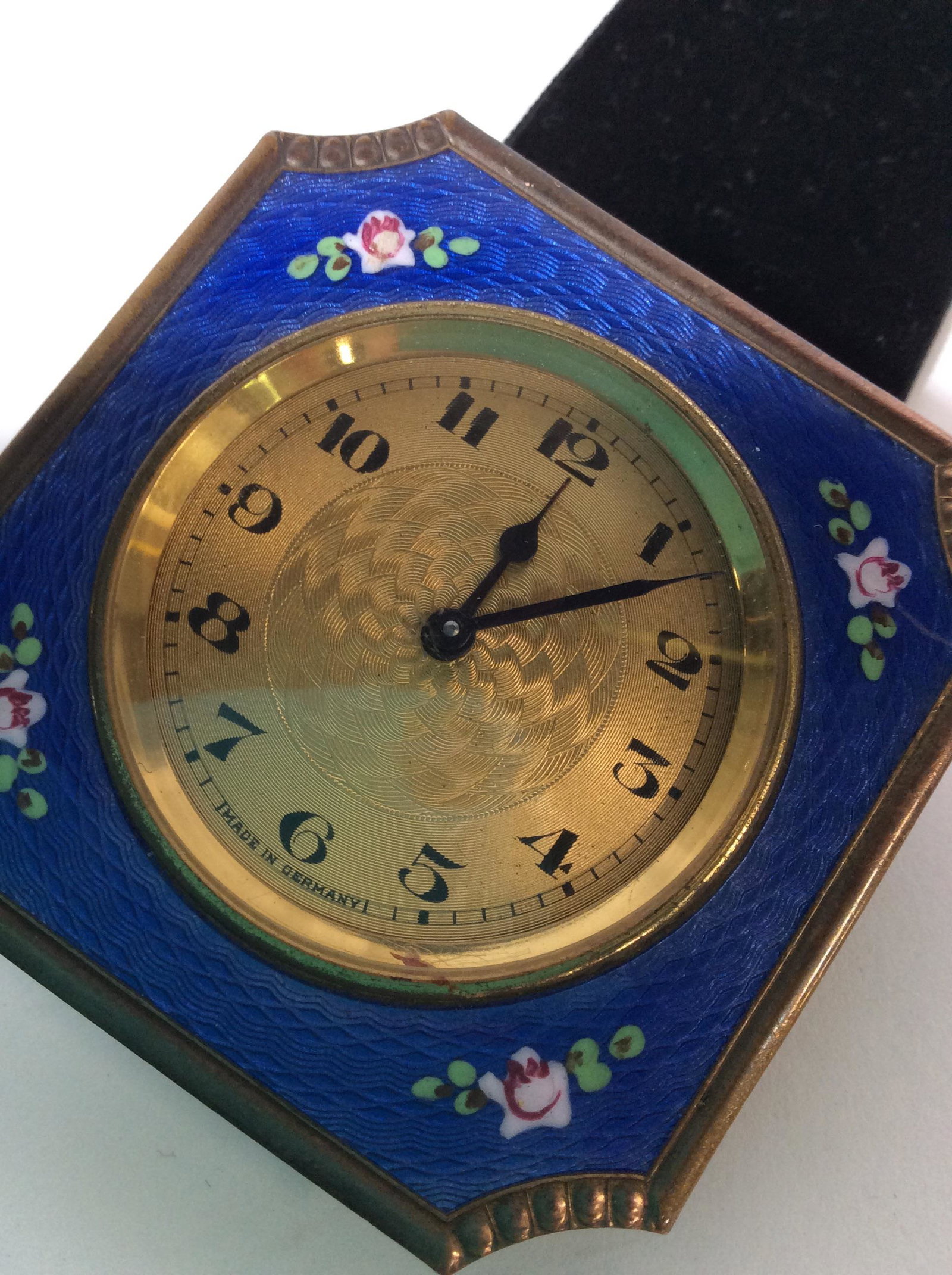 Antique European Enamel Clock, Germany: Border Florals On Blue background, Brass Clock face. Backside and under glass read MADE IN GERMANY. Velour sash attached w/ matching hanging accessory. Wind up. Clock ticks. Needs repair for hands dia