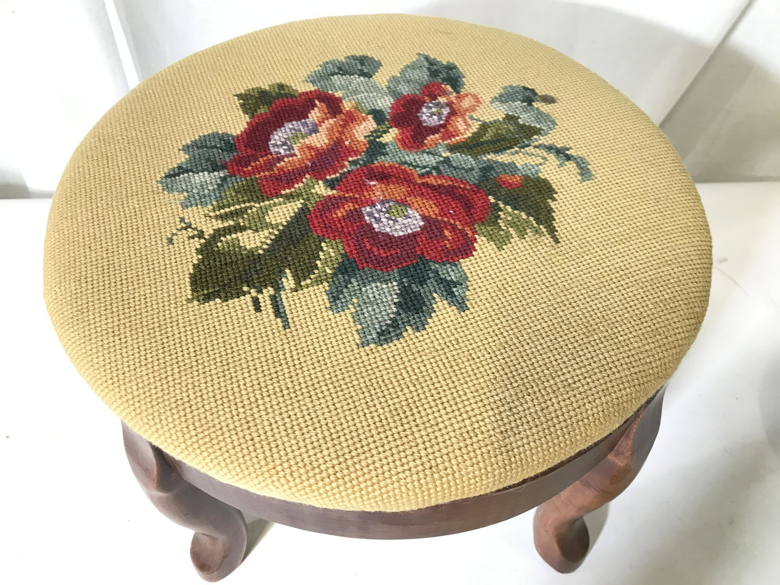 Vintage Carved Wooden Needlepoint Footstool: Footstool has carved wooden legs. Top of piece is needlepoint with multi toned floral and leaf detail. Piece measures approximately 10 inches tall 14 inches diameter. Footstool, vintage footstool, woo