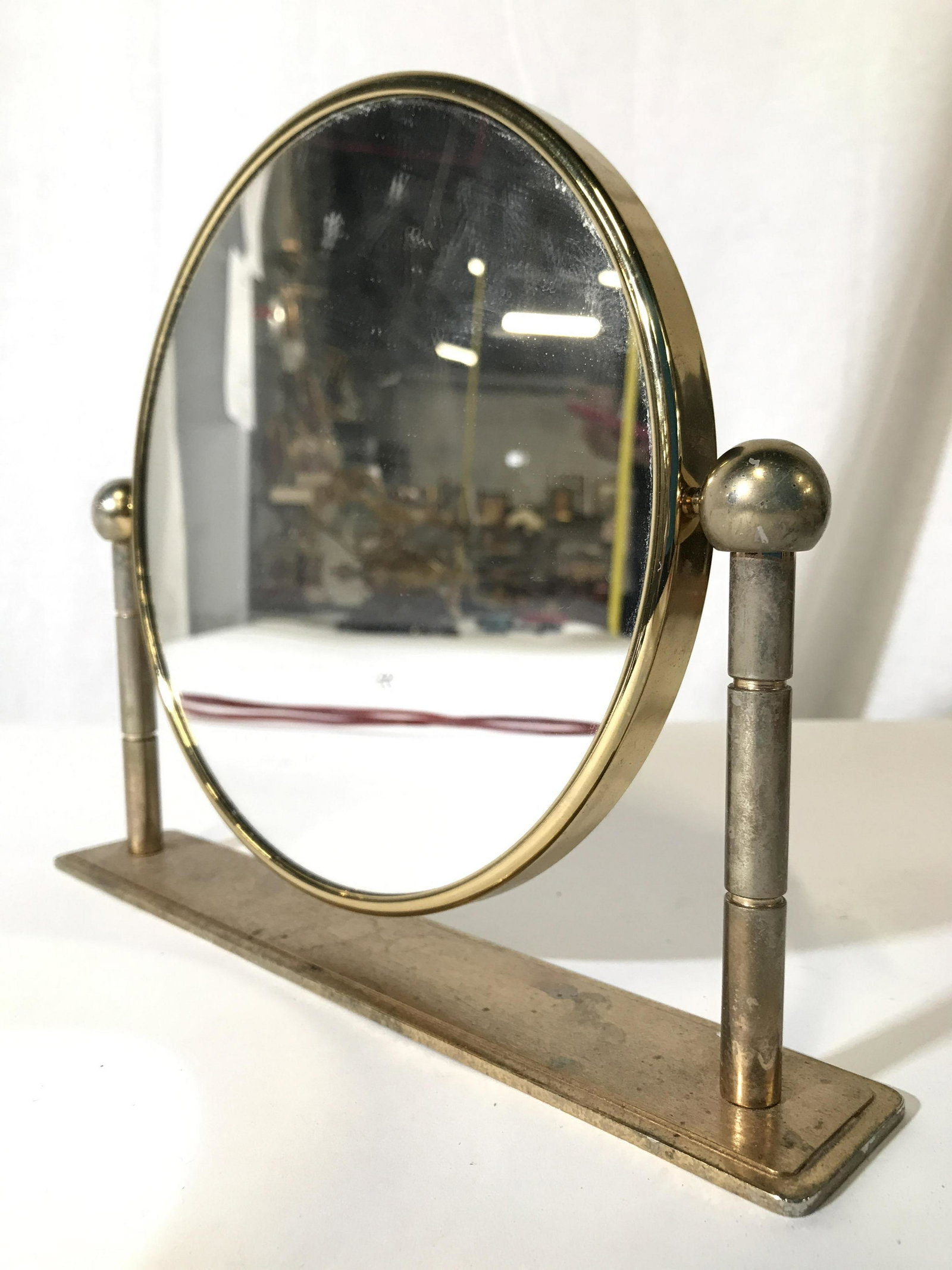Brass Double Side Magnification Flip Mirror: Mirror has circular shape. Mirror rotates on horizontal axis. Piece is gold toned and appears to be brass. Piece measures approximately 8 inches tall 10 inches wide. Mirror, flip mirror, double sided 