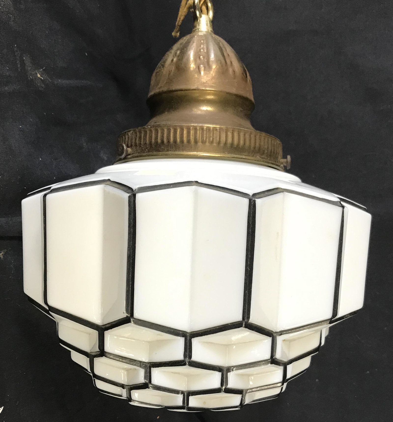 Antique Glass Pendant Light: This piece is an antique pendant light. The light bulb is Held in a glass housing, the housing is crafted to resemble a polyhedron or crystalline shape. The detailing on the housing is brought out thr