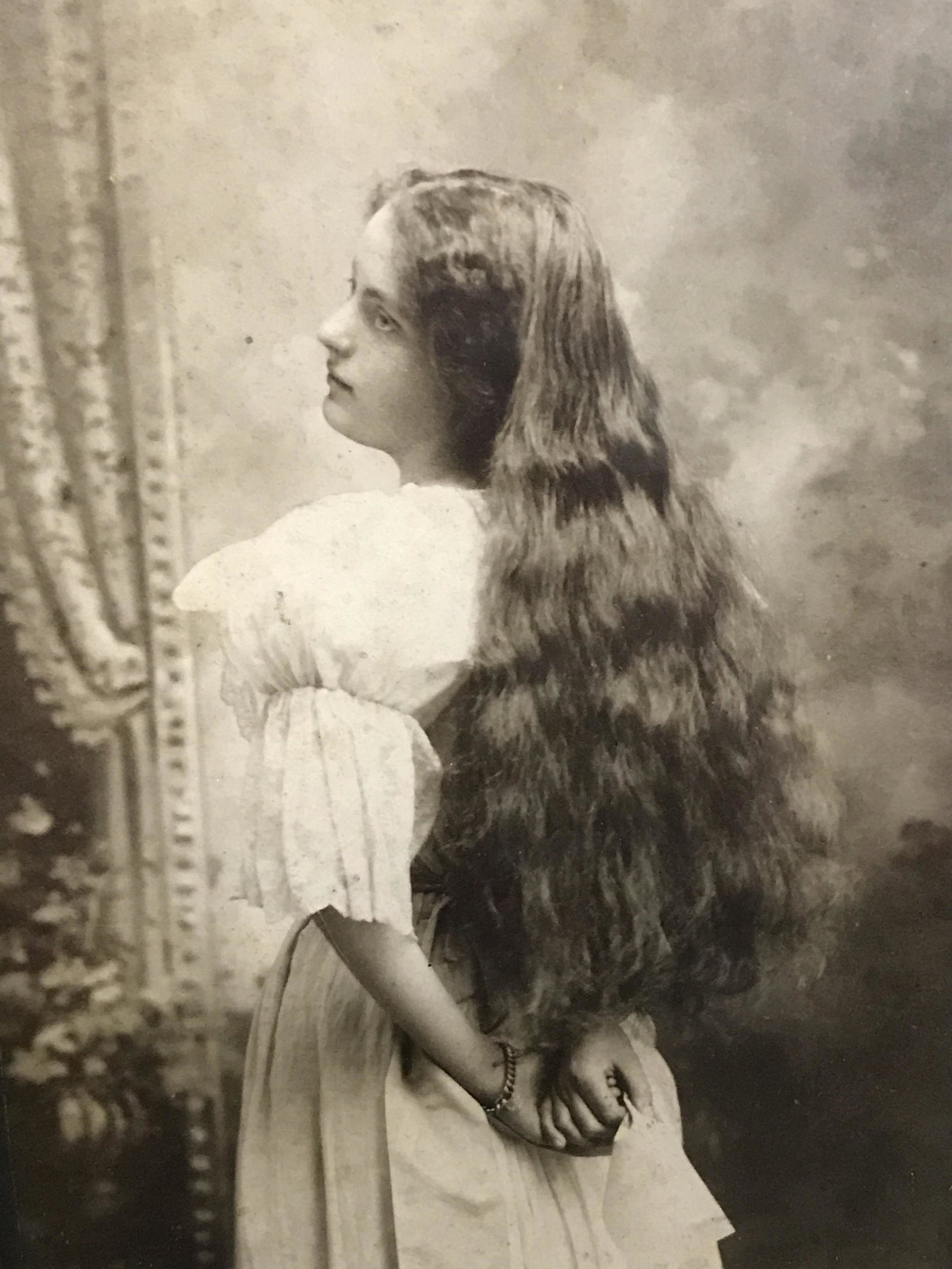Early Black and white portrait photograph: Early black and white photograph documenting a young woman in white with her hair down, turned at three quarters to show her face, her dress and her long hair, twin reflex medium format, frame is silv