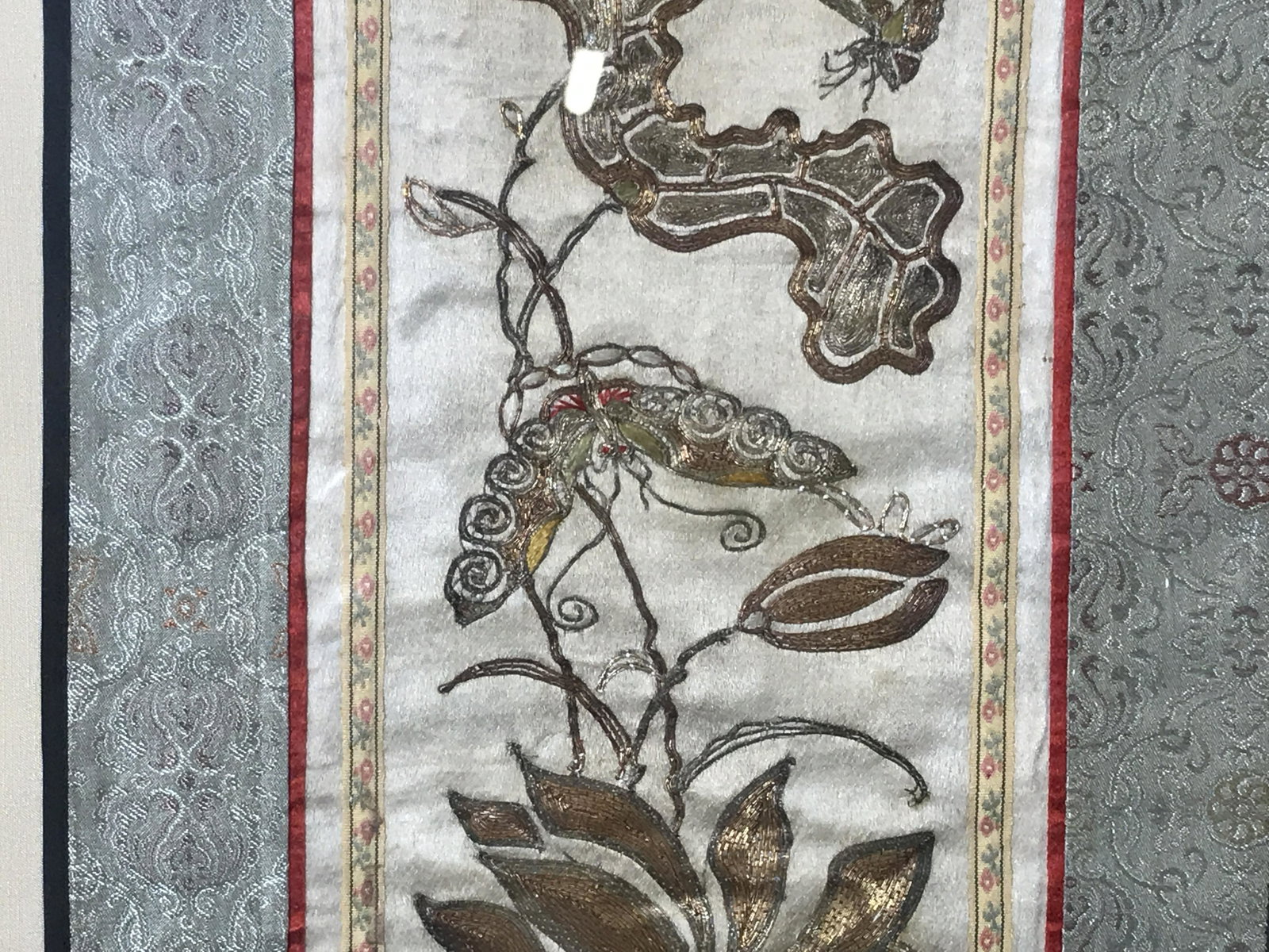 Framed Embroidered Fabric: Framed embroidered fabric, subject blue floral patterned possibly satin fabric with a center section of champagne colored satin with metallic gold embroidery of butterflies and flowers, on tan fabric 