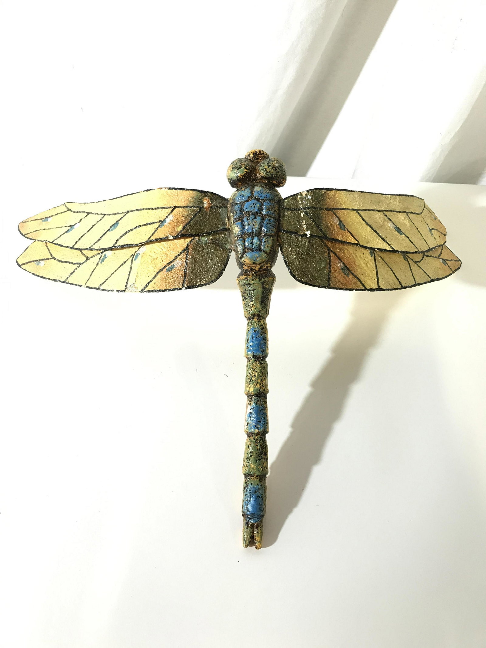 Decorative Dragonfly Wall Sculpture: This piece is a decorative dragonfly sculpture. The piece is hand-painted. The wings are crafted from metal, the body appears to be crafted from stone or a composite material. The piece measures appro