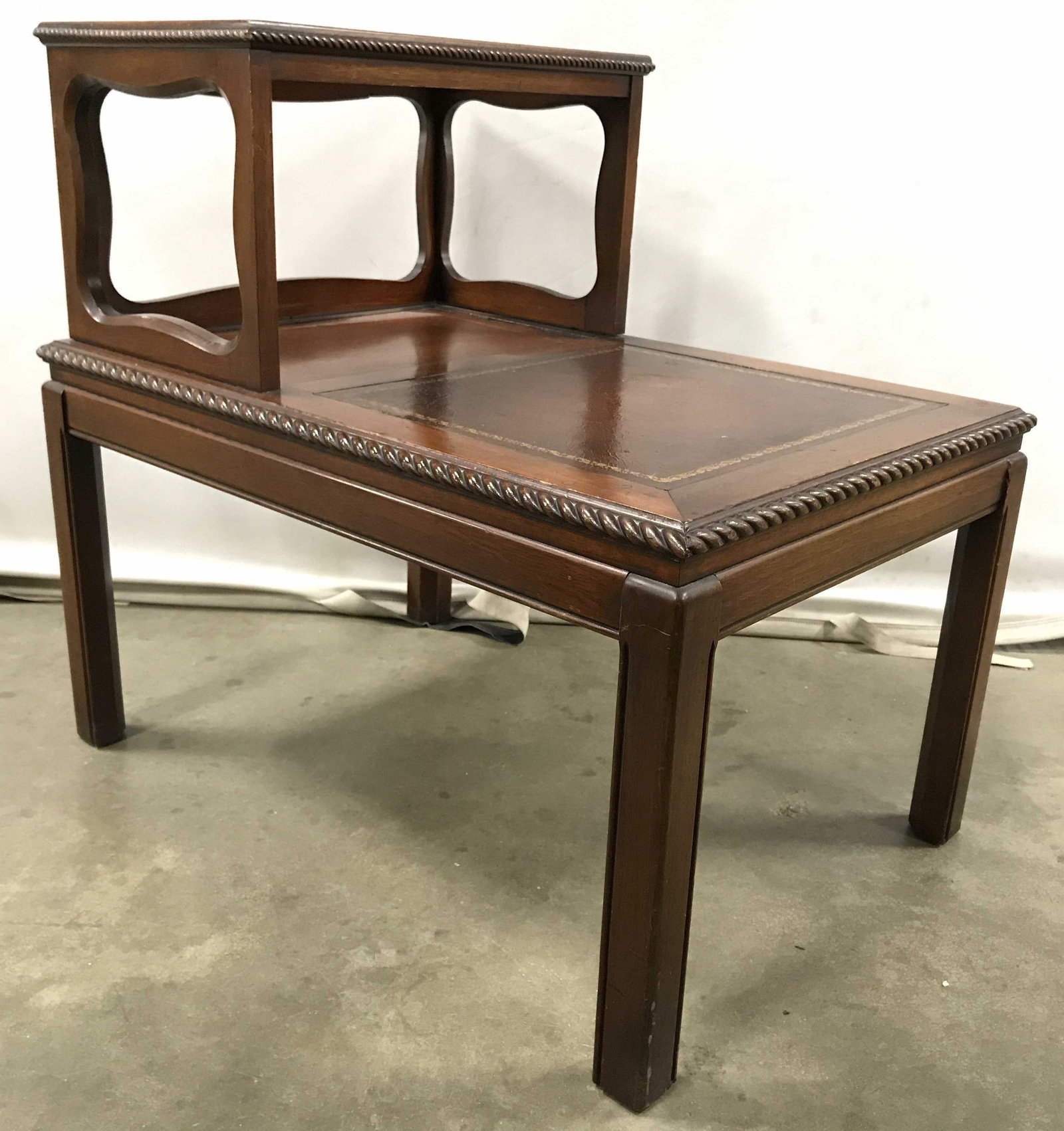 Vintage Carved Wooden Leather Top Side Table: Side table is vintage and wooden. Piece has brown toned leather top with ornate gold toned detail. Table has 2 levels. Table is Possibly mahogany. Piece measures approximately 28 inches long 26 inches