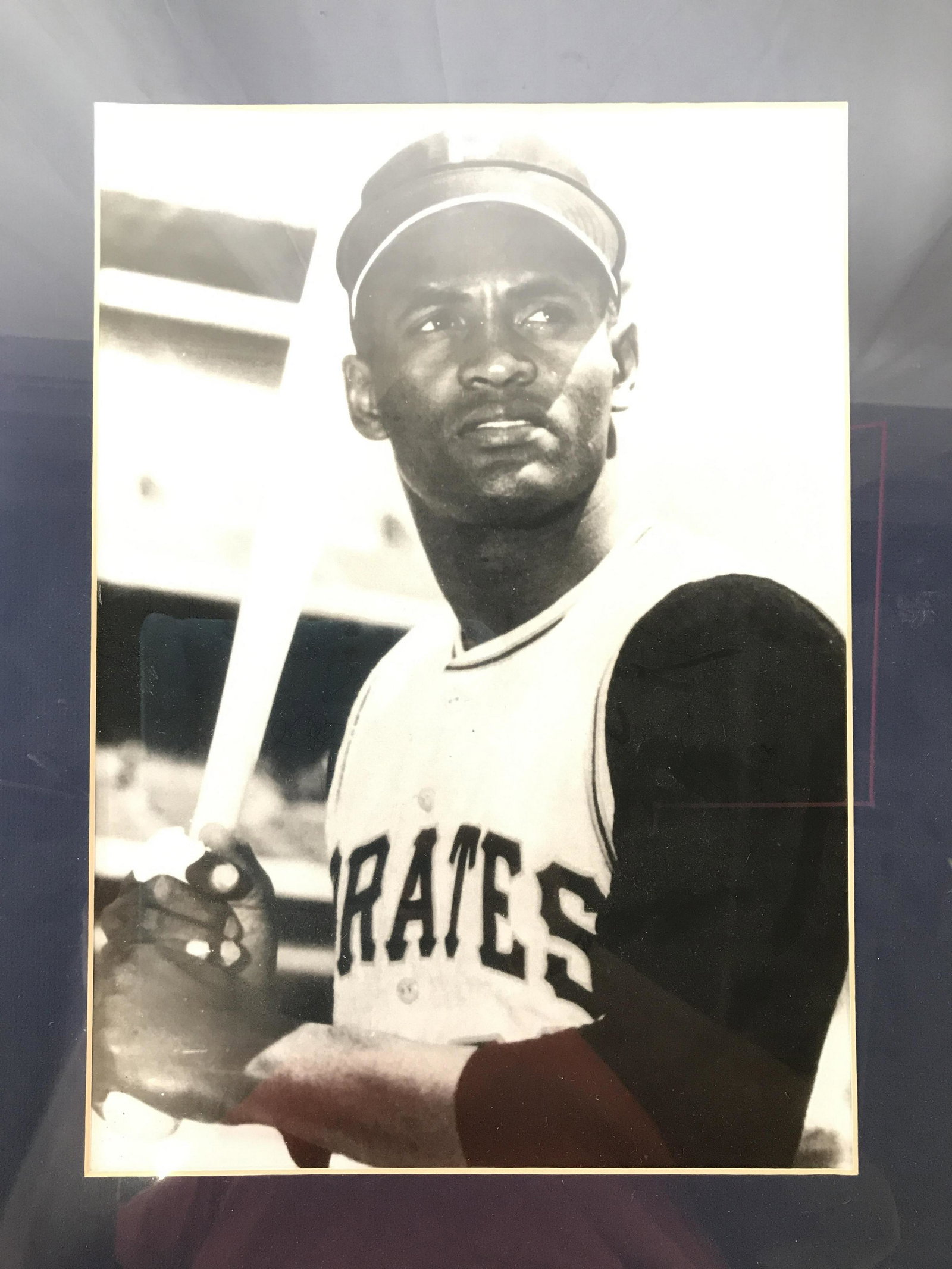 Framed Roberto Clemente Photographic Print: Print depicts late Major League Baseball Player Roberto Clemente. Print is black and white. Piece is professionally framed and matted with brown and black toned frame. Piece measures approximately 18.