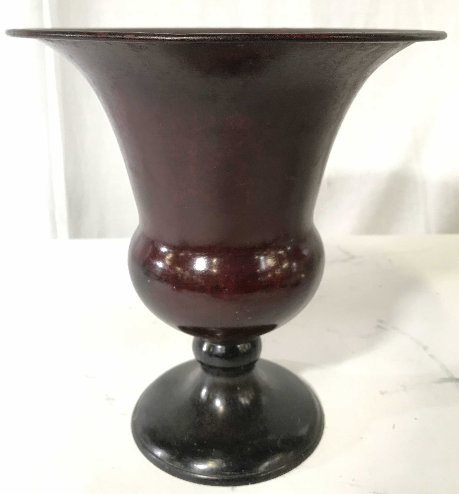 Red Toned Metal Trophy Urn: Urn has dark red and black tones. Piece is metal. Urn has trophy shape. Piece measures approximately 9 inches tall 8 inches wide. Urn, Metal urn, trophy urn, trophy style urn. vase, vessel, tableware,