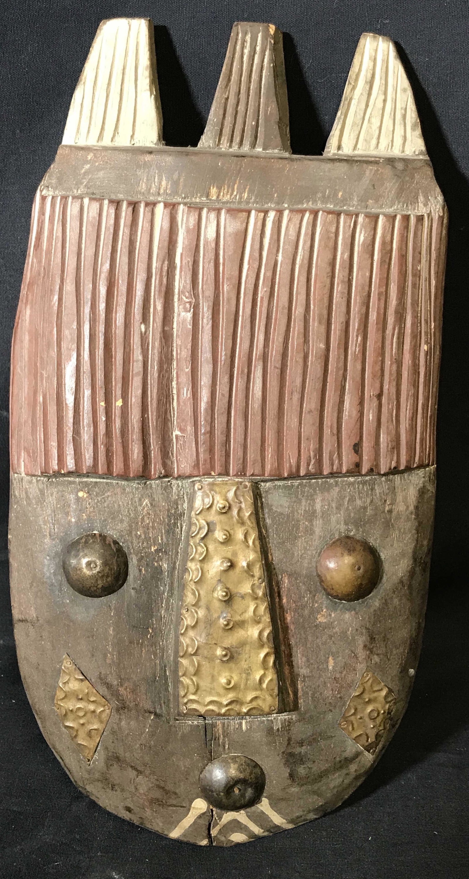 Decorative Wall Mask, home decor: Decorative wall mask, wooden with metal embellishments, painted in red black and white, hand carved from one wood block, Chip to reverse where a hook was once placed, done in a primitive nature, measu