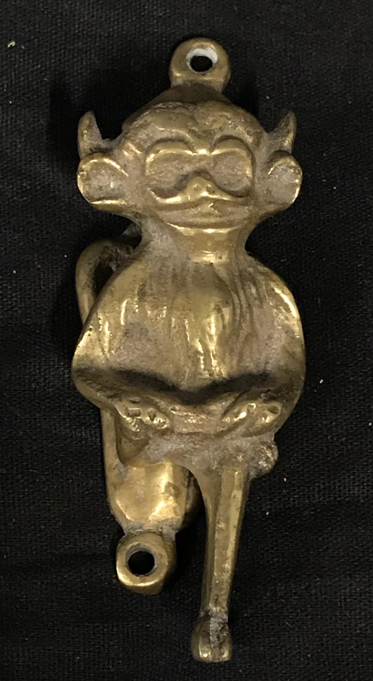 Gold Toned Metal Door Knocker: Gold toned metal door knocker, two holes in knocker backing for screws, knocker takes the shape of a monkey sitting with their legs crossed and horns protruding from its head, some fade to gold tone, 