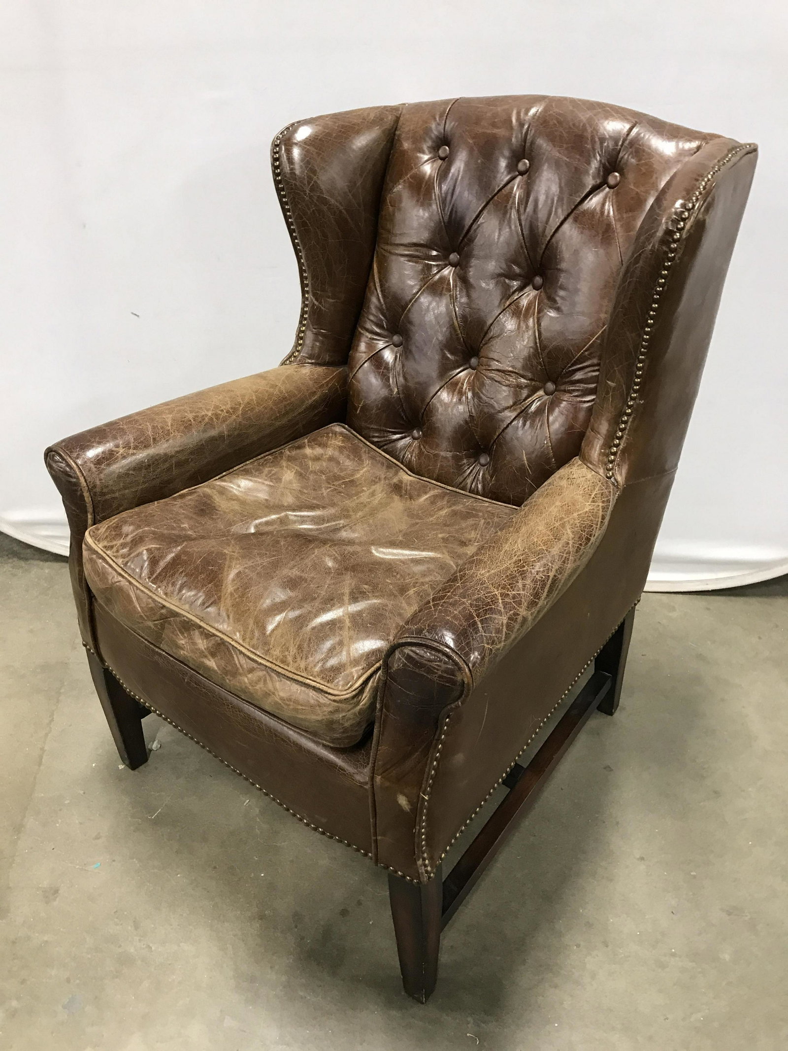Antique Tufted Leather Armchair WHITE X WHITE: Tufted leather wing chair, Wing chair, This piece is a possibly vintage, possibly antique, leather wing chair, armchair. The legs are joined by an h stretcher, and the back of the chair is button tuft
