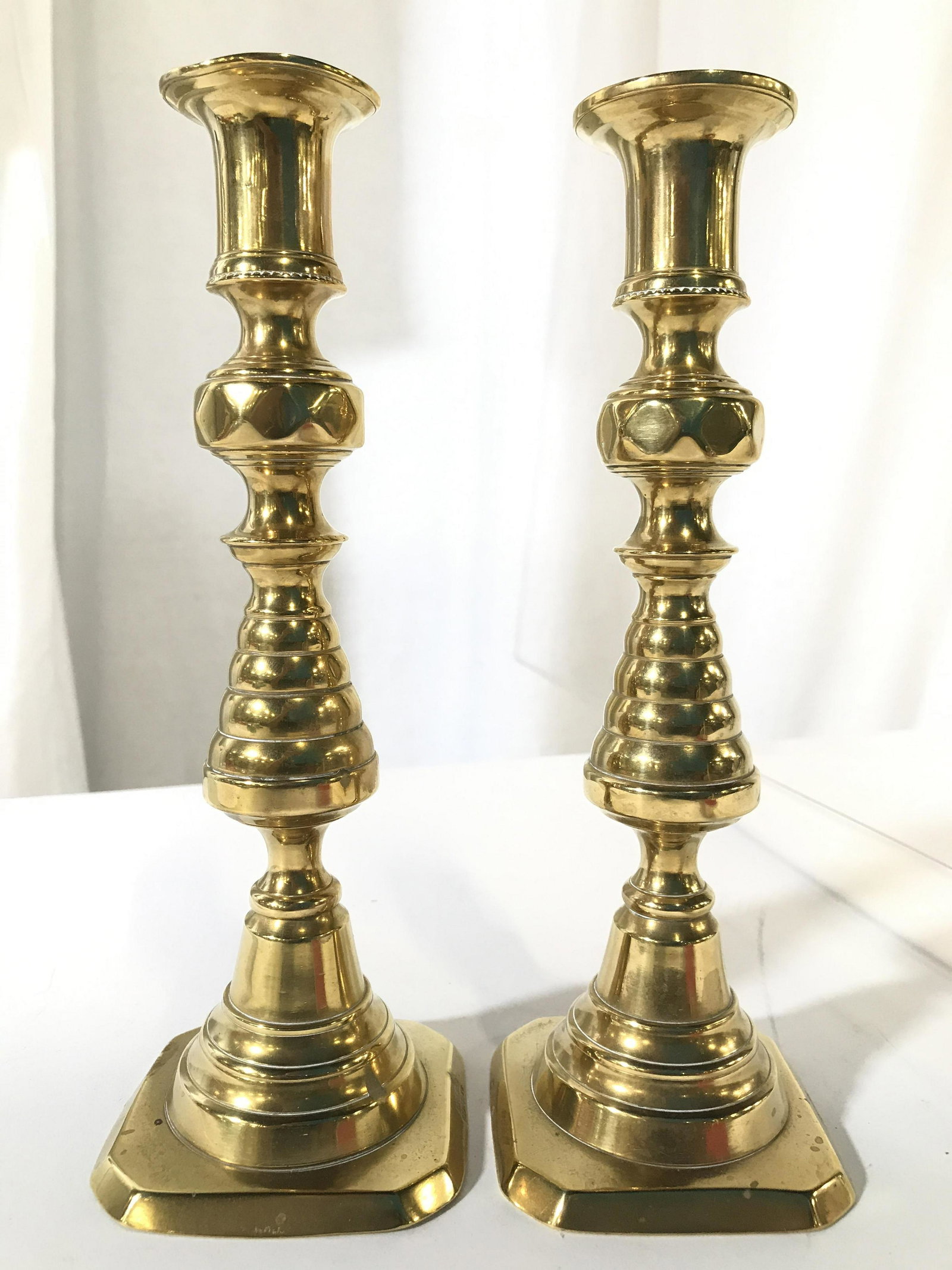 Pair Gold Toned Candlesticks: Lot includes 2 candlesticks. Each are marked ENGLAND at base. Each are gold toned, possibly brass. Each measures approximately 9 inches tall 3 inches deep and wide. Brass candlesticks, pair candlestic