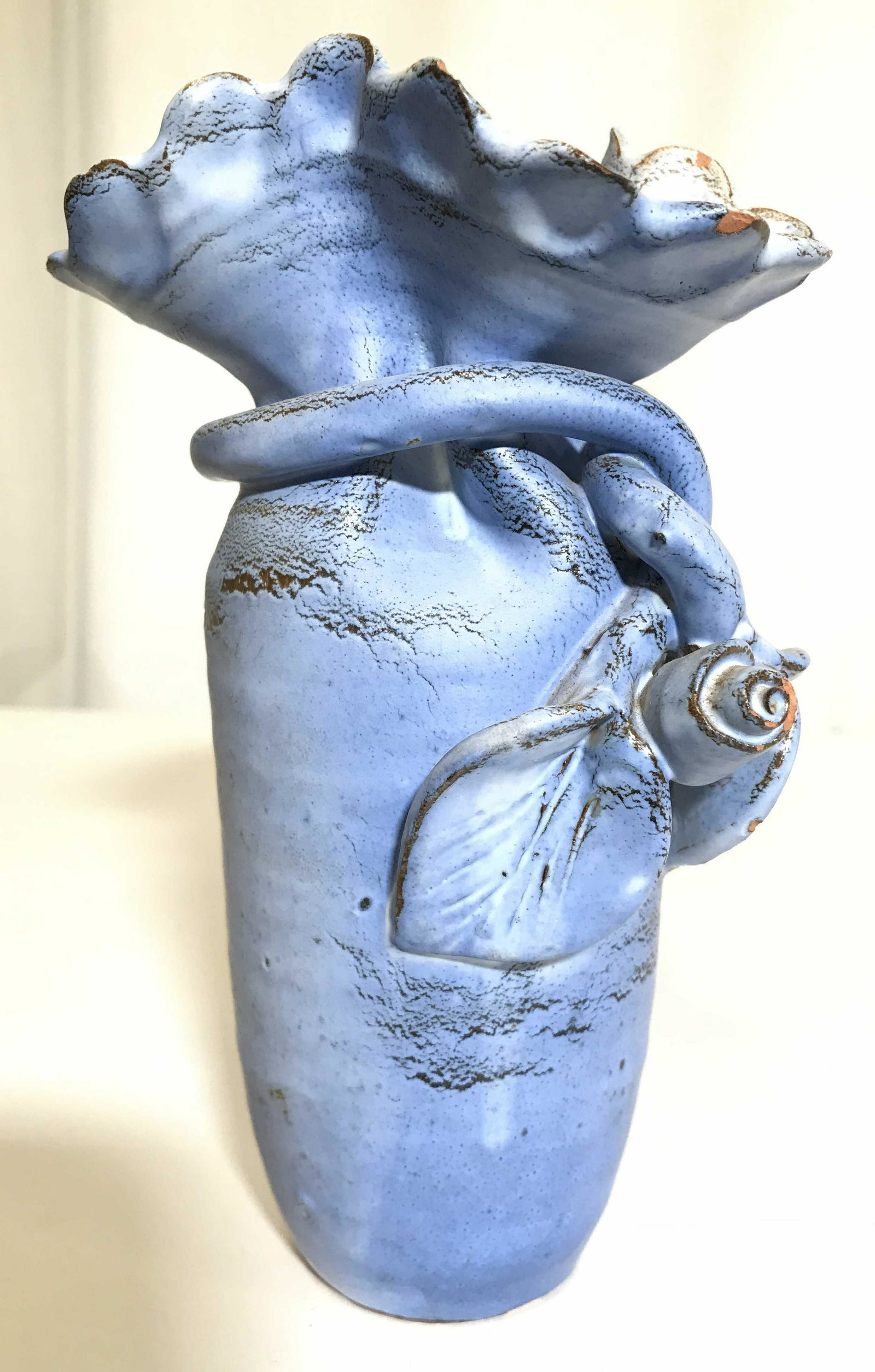 Vintage Ceramic Frilled Rim Vase: Vase is light blue toned and ceramic. Piece has a frilled rim. Vase, ceramic vase, vessel, ceramic vessel, frilled rim vase. tableware, tabletop accessories, Vase has leaf and vine detail which wraps 