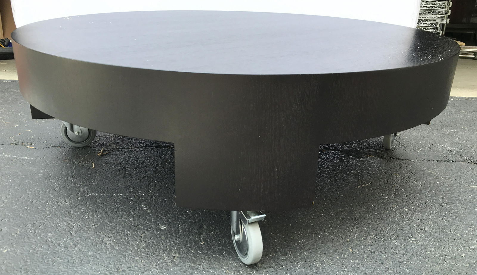 MINOTTI Black Toned Wooden Coffee Table On Casters: MINOTTI . Coffee table is black toned. Piece has circular shape. Piece is wooden. Table sits on 4 black toned wheels. Measures approximately 55 inches wide 18 inches tall. Coffee table, wooden coffee
