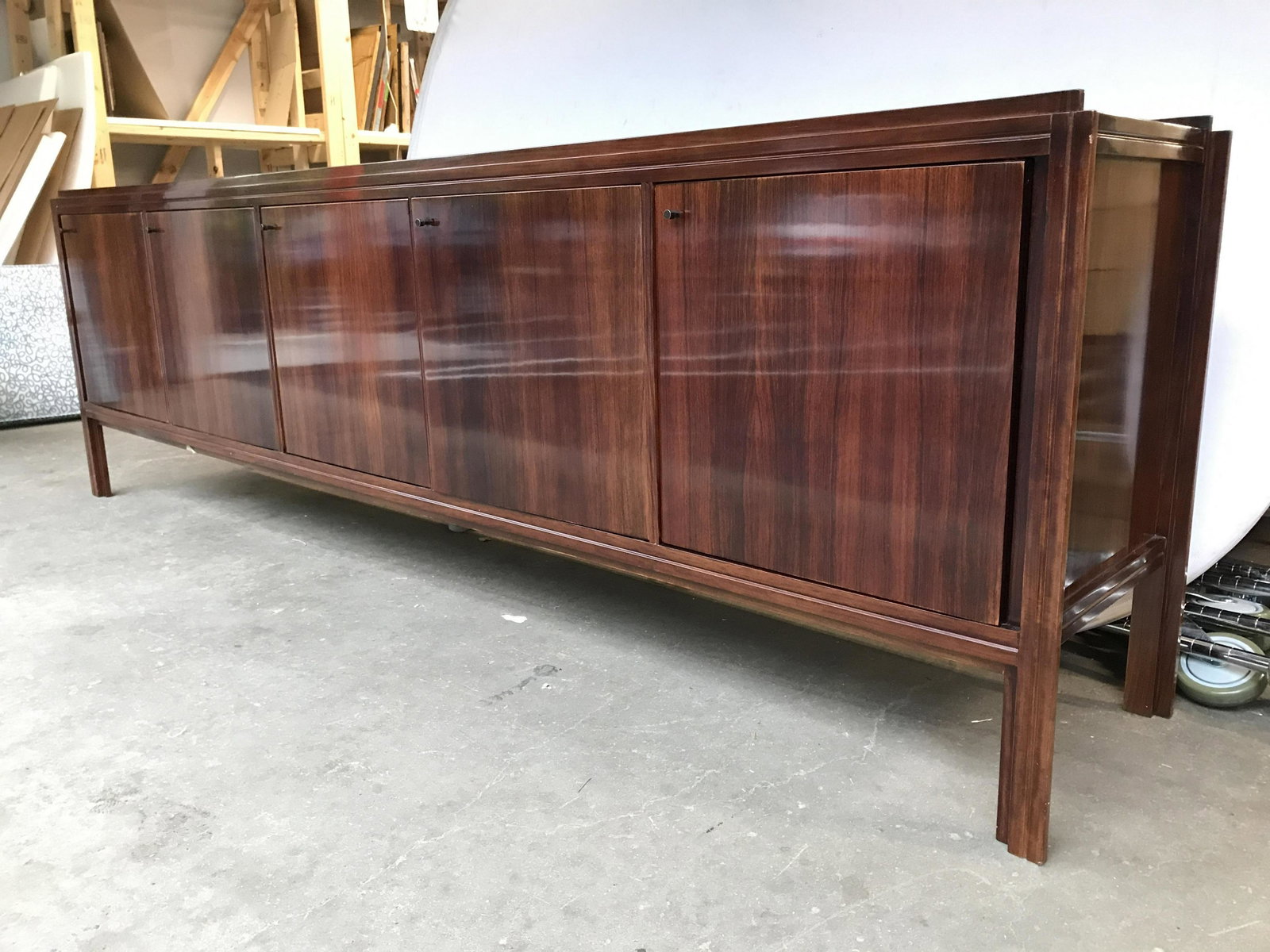 Mahogany Toned Wooden Buffet Table: Buffet table is wooden. Piece Contains 5 cabinet doors. 1 cabinet door has 3 drawers inside. Tabletop is raised in front and backside. Each cabinet space has 1 shelf inside. Cabinet doors have petite 