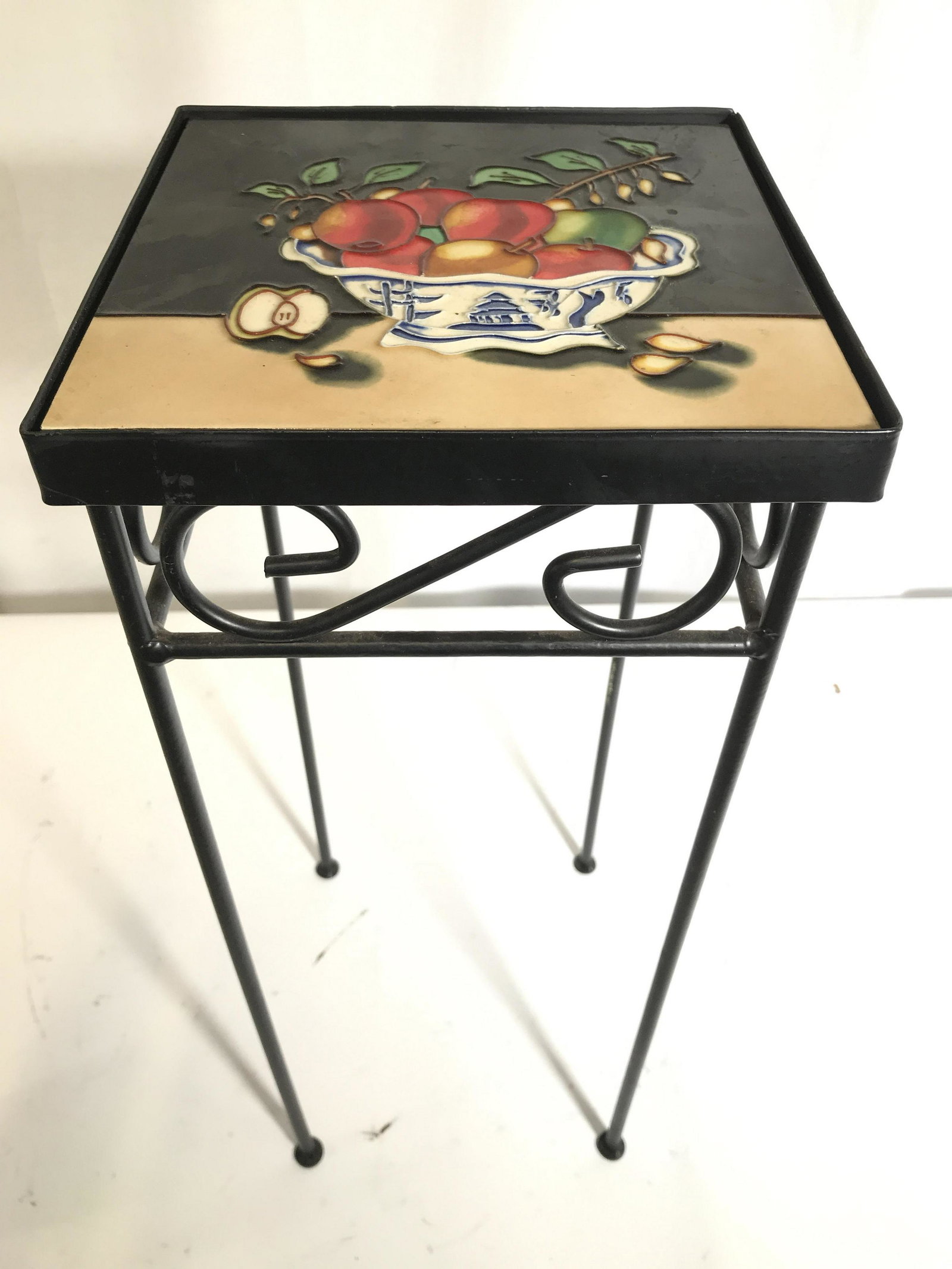 Metal Tile Top Plant Stand / Side Table: Table frame is black toned and metal. Piece has s curve detail. Table top is tiled with bowl of fruit detail, possibly hand painted. Piece measures approximately 20 inches tall 8 inches square. Plante