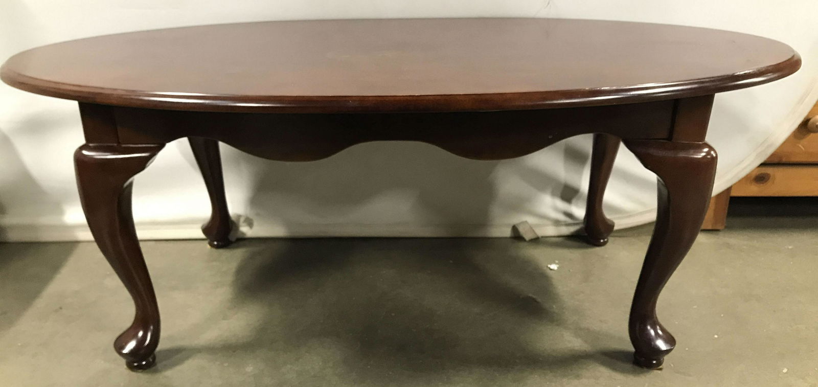 THE BOMBAY Company Cabriole Leg Coffee Table: Underside of tabletop is marked, THE BOMBAY COMPANY. Coffee table is brown toned and wooden. Piece has oval shaped top and carved wooden Cabriole leg. Measures approximately 46 inches long 26 inches d