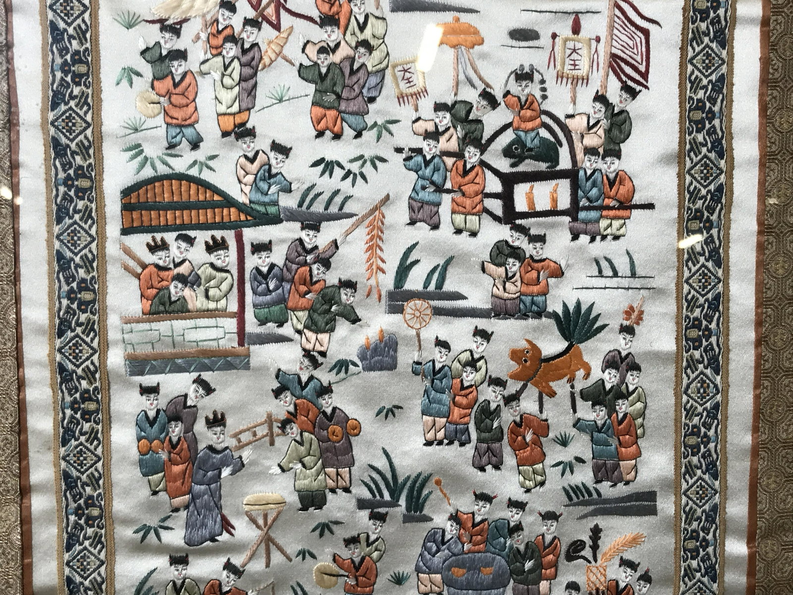 Hand Embroidered Chinese Tapestry: Hand embroidered Chinese tapestry, no apparent signature, subject depicts various children together playing different games, scene is bordered in blue geometric symbols and a second border of a gold t
