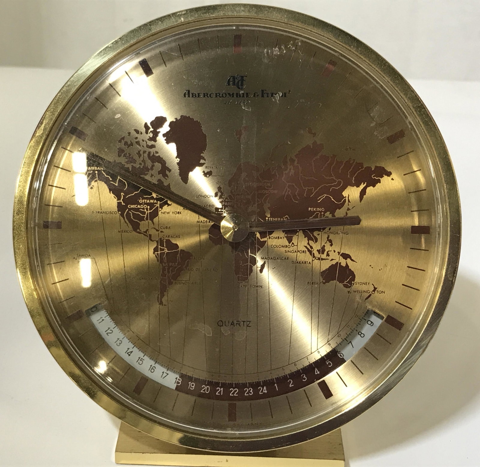 Kienzle Abercrombie & Fitch Clock, world map: Kienzle Abercrombie & Fitch clock, made in a gold toned metal with burgundy accents, clock displays a world map with major cities pinpointed And time zones coordinated at the bottom, major text on fac