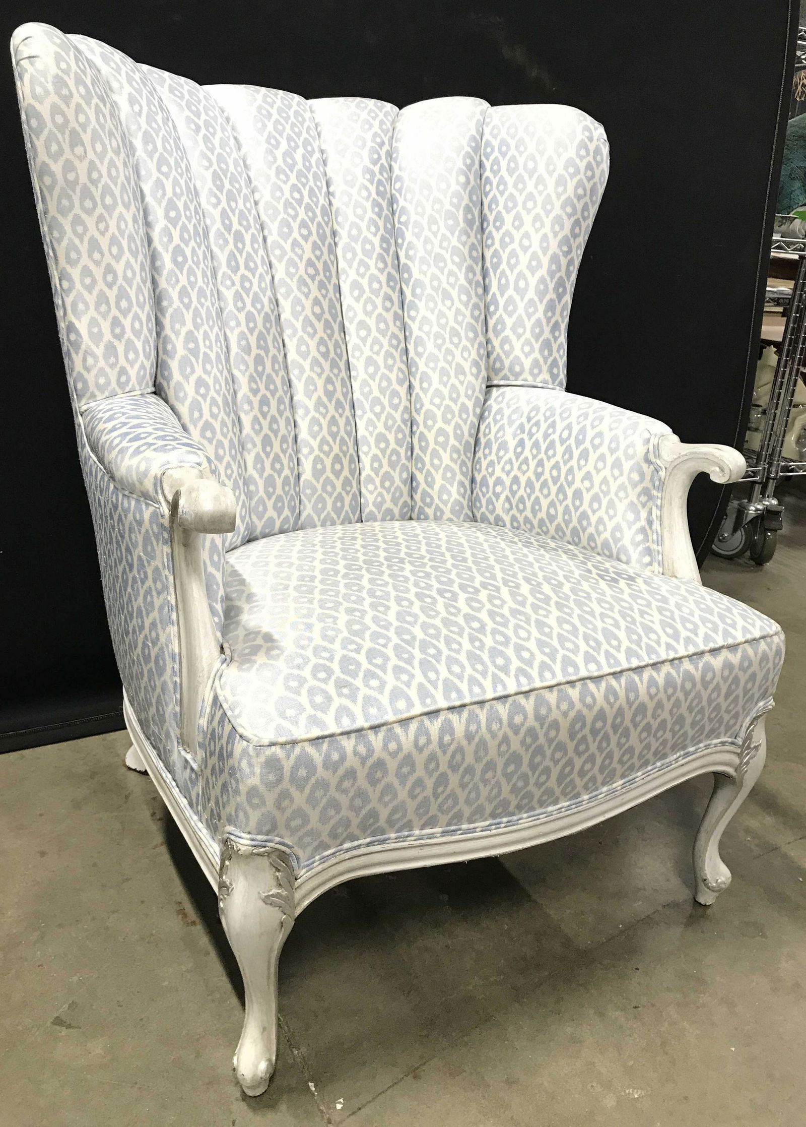 Vintage Double Welted Upholstered Wingback Chair: Wing chair is vintage. Piece has white and light blue toned patterned upholstery. Piece has carved wooden feet and arm rest ends. Chair near base has double welting. Wing chair, wing back chair, armch