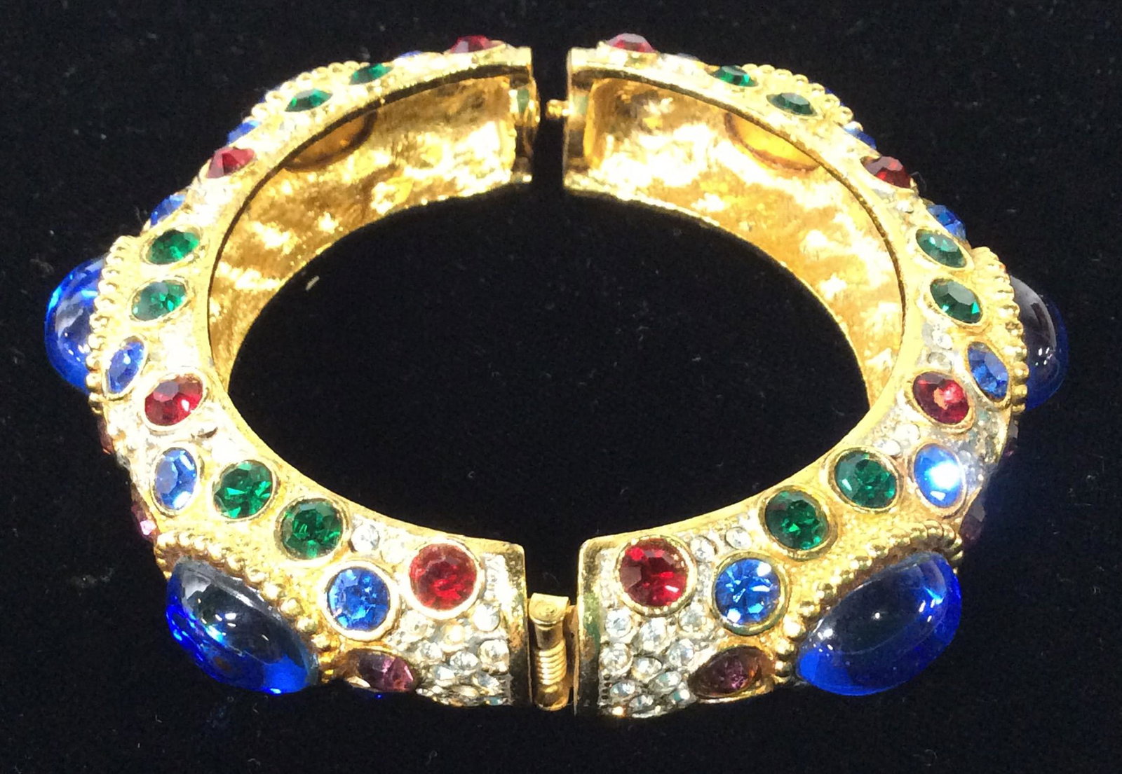 Bejeweled Rhinestone Cocktail Bangle Bracelet: Elaborate Bangle full of multi colored rhinestone all bezel set, and smooth blue toned cabochons. Hinges open and snaps closed. Appears to read ‘Spain’ . Diameter 2 in for wrist. Costume Jewelry, 