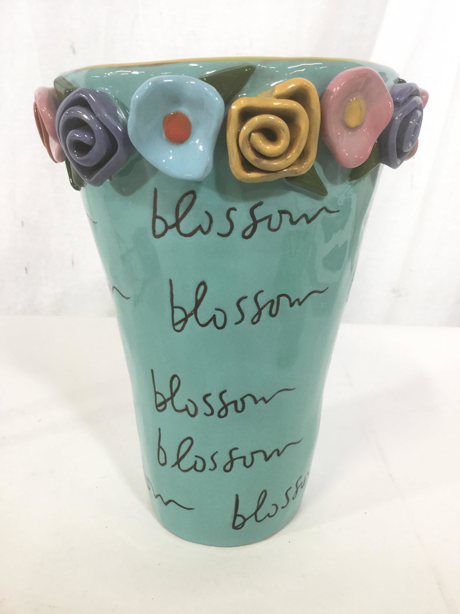 Hand Painted Earthenware Flowerpot: This is a Handpainted Earthenware flower pot. The pot is colored in aqua blue tones, a number of flowers adorn the rim of the pot, and the word blossom is written across the pot’s surface. The inter