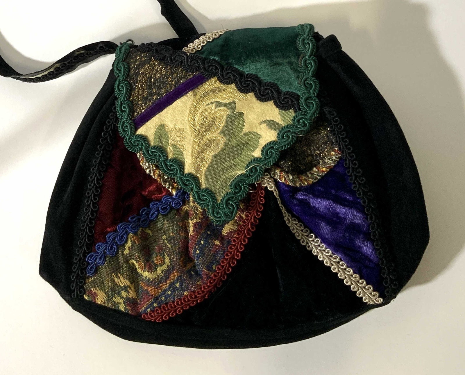Suede and Appliqué Handbag: Suede handbag with front button snap closure, the front of the bag has an over the top enclosure, that has been adorned with different swatches of upholstery fabric separated by stripes of different c