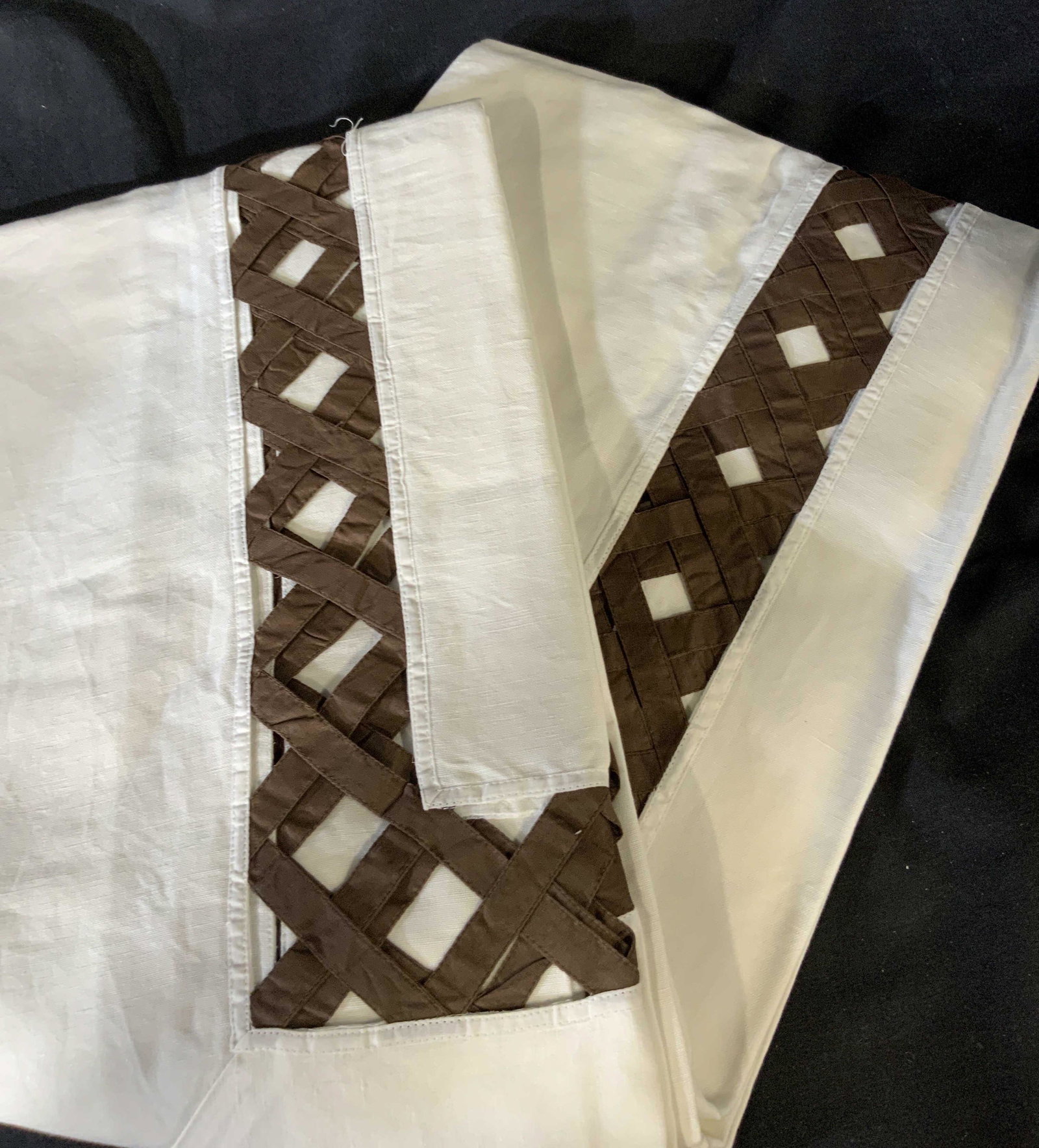 Set of Two Decorative Tablecloths: Set of two large table clothes in white with a brown peek-a-boo basket pattern around the edge of the table where it hangs over the side of the table, made of linen the basket pattern is in a coffee b